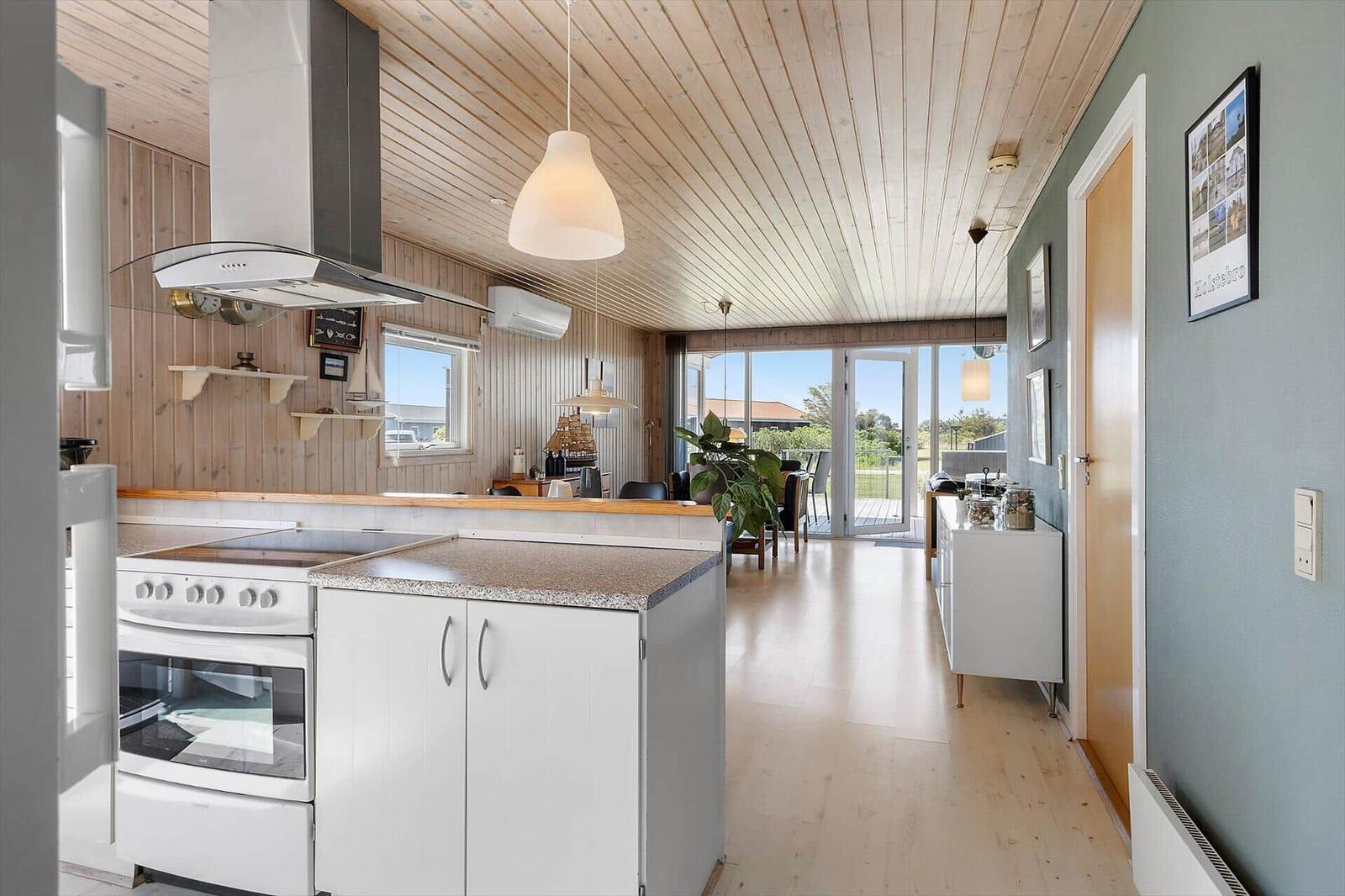 Küche mit Arbeitsplatte, Herd und Dunstabzug. Durchgang zu Wohnbereich mit Balkon.
