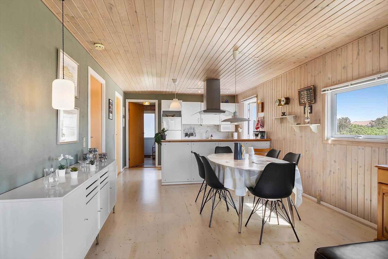 Küche und Essbereich mit Holzdecke und -wänden. Tisch mit Stühlen, Fenster, Küchenzeile.