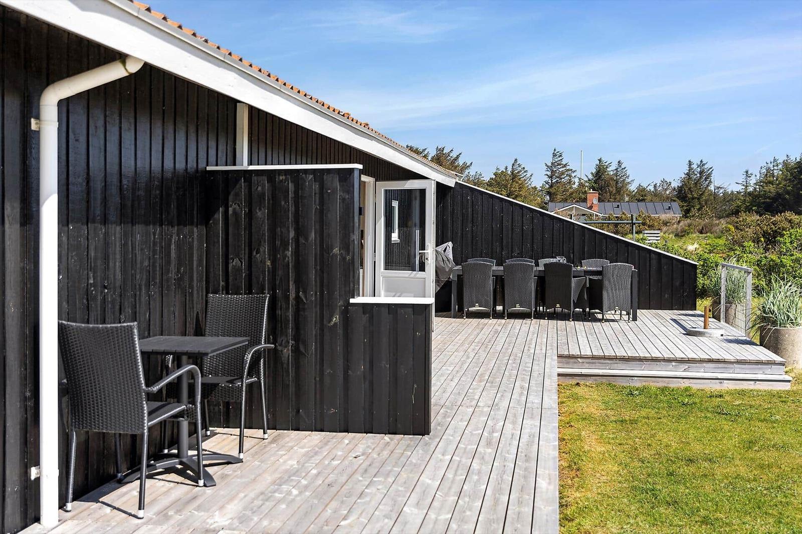 Terrasse mit Tisch und Stühlen neben einem schwarzen Holzhaus mit weißem Dachrand.