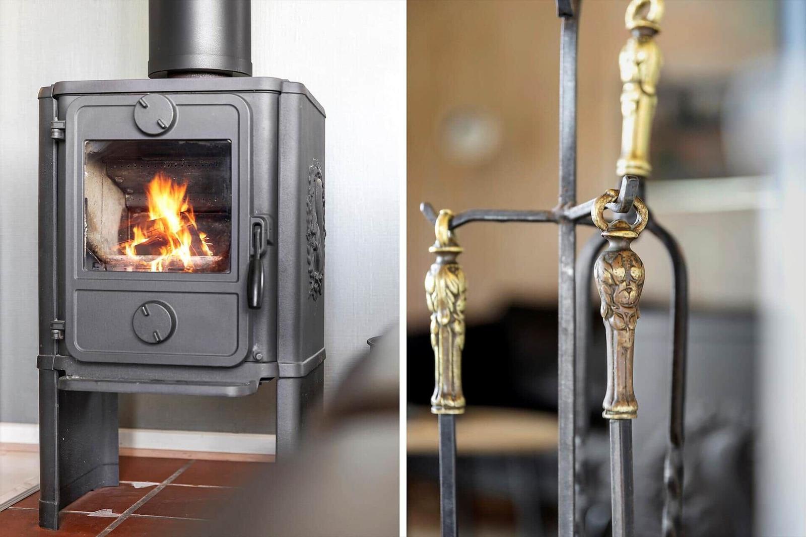 Kaminofen mit brennendem Holz und goldverzierte Feuerzeugen.