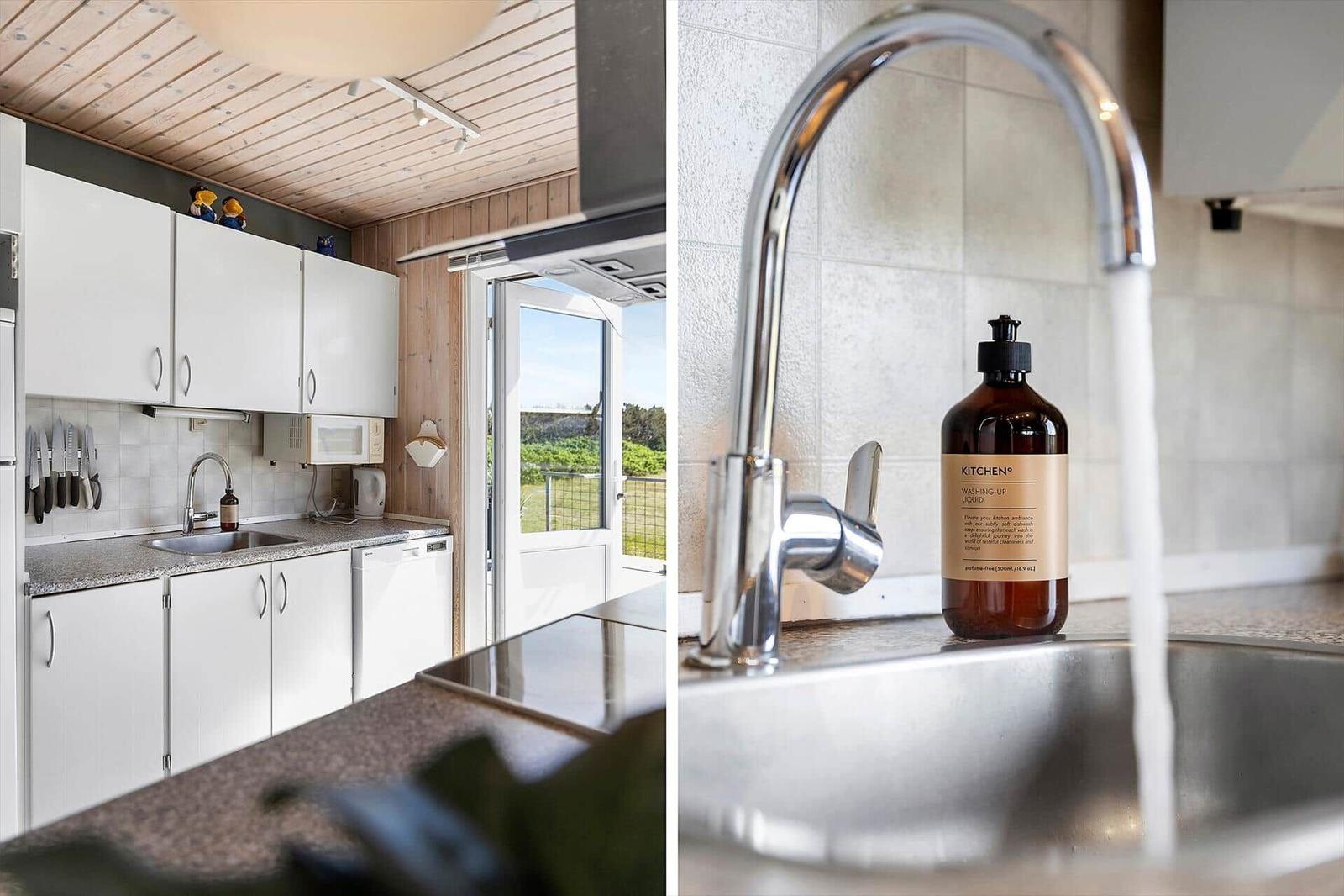 Küche mit weißen Schränken, Spüle und Blick auf Garten. Wasserhahn mit Flasche.