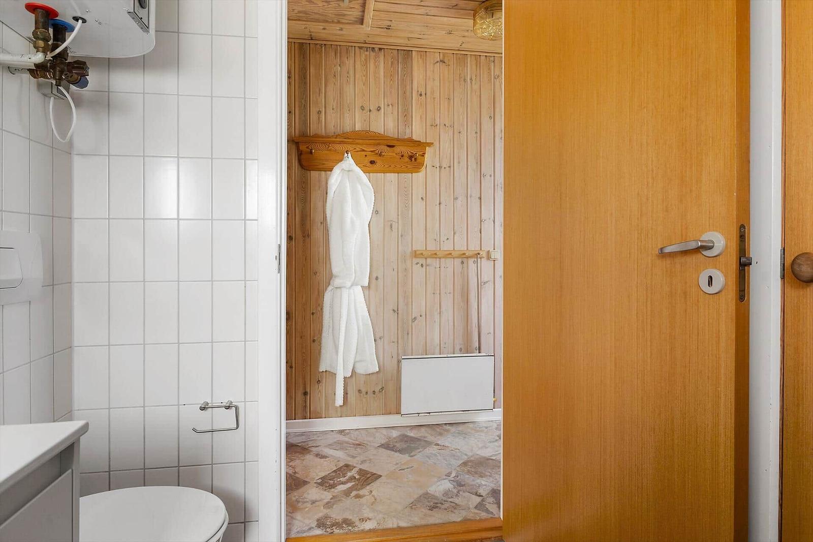 Badezimmer mit Toilette und angrenzender Dusche mit Holzwand und Bademantel