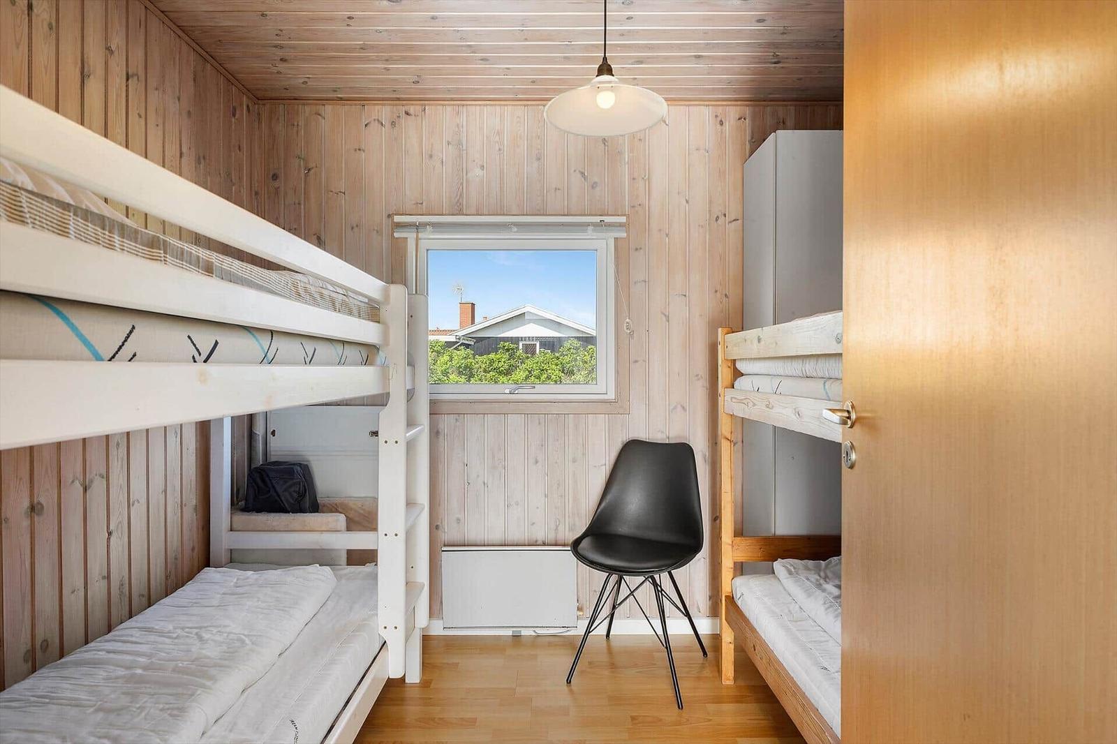 Zimmer mit zwei Etagenbetten, Fenster und schwarzer Stuhl.