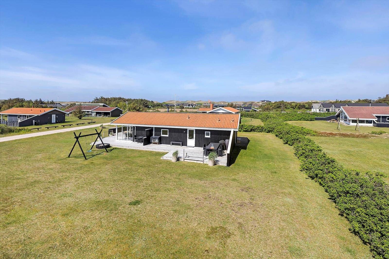 Schwarze Ferienhaus mit orangefarbenem Dach und großem Garten. Spielplatz und Terrasse vorhanden.