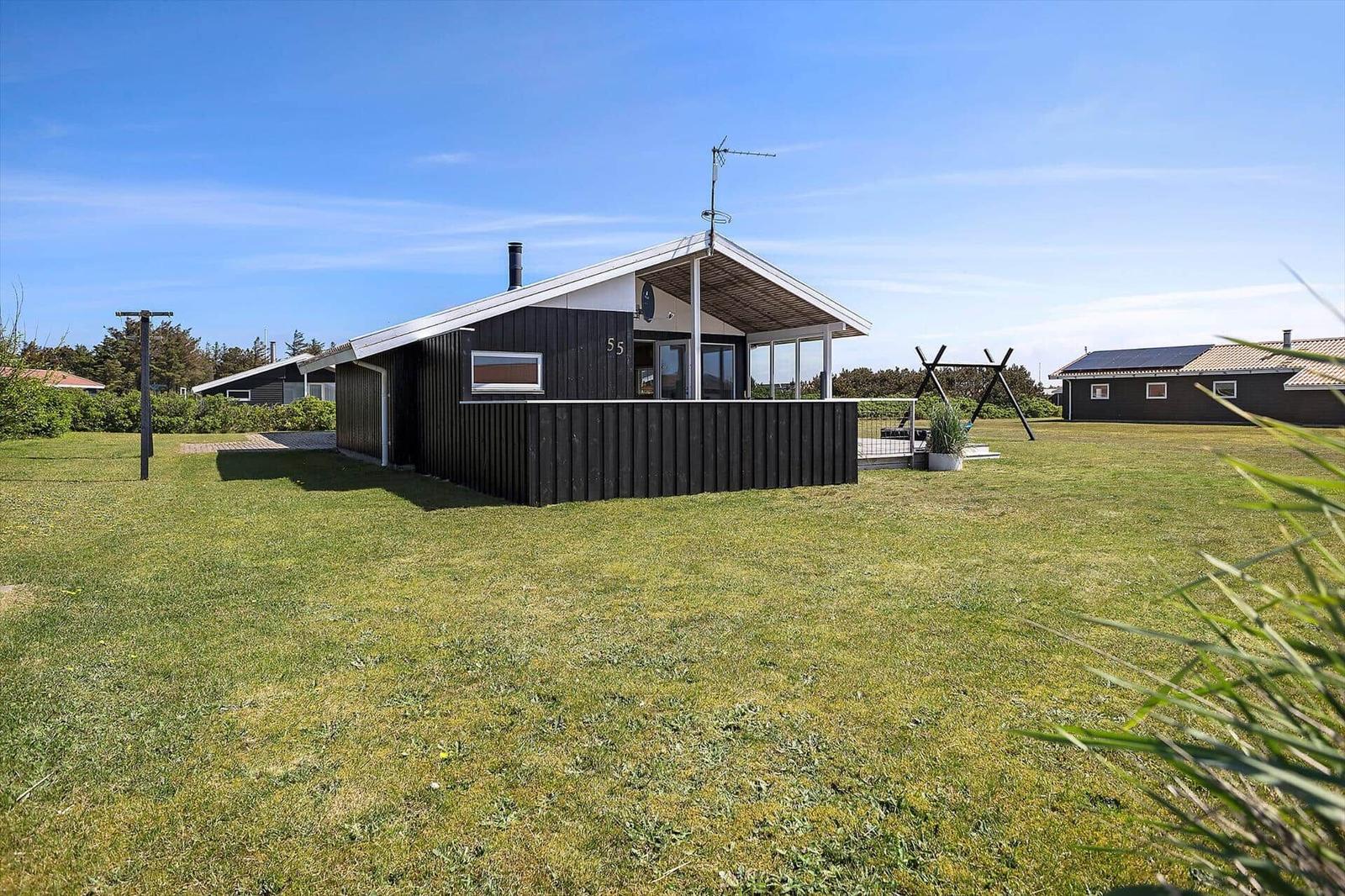 Moderne Holzhütte mit Terrasse und Garten. Hausnummer 55. Blick auf grünen Rasen und Nachbarhäuser.
