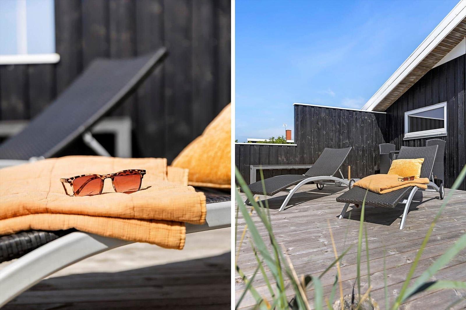 Terrasse mit Liegen, Kissen und Sonnenbrille. Holzterrasse und schwarze Fassade.