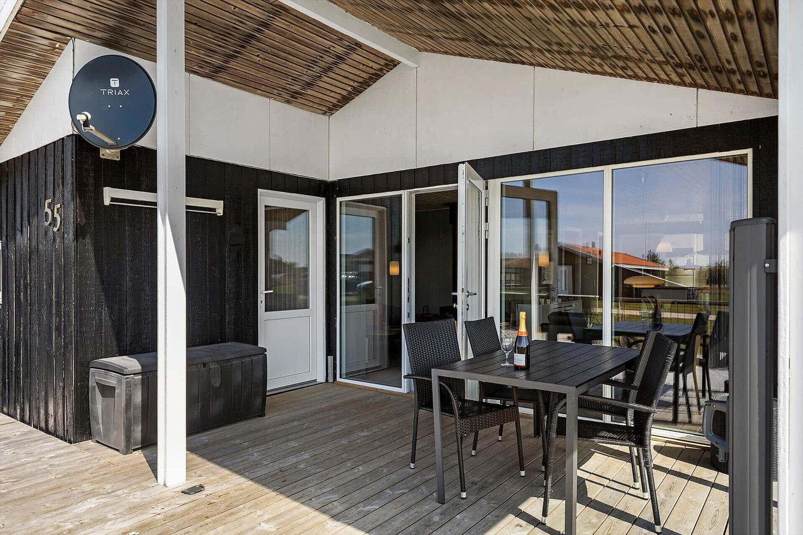 Terrasse mit Tisch und Stühlen, Schiebetür zum Innenraum, Holzdecke und Satellitenschüssel.