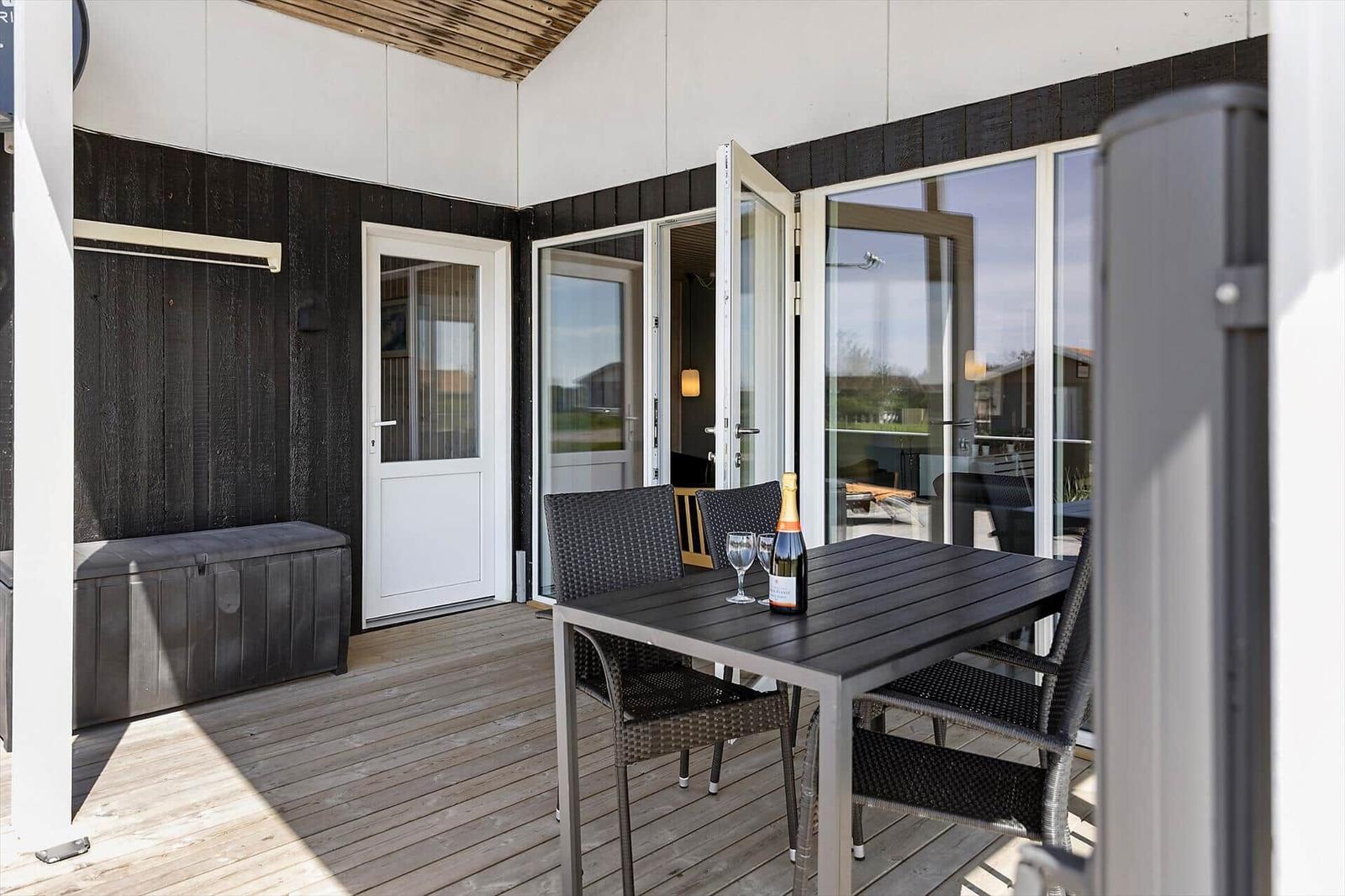Terrasse mit Tisch, Stühlen und Flasche Champagner. Hintergrund: Haus mit Glasfront und Tür.