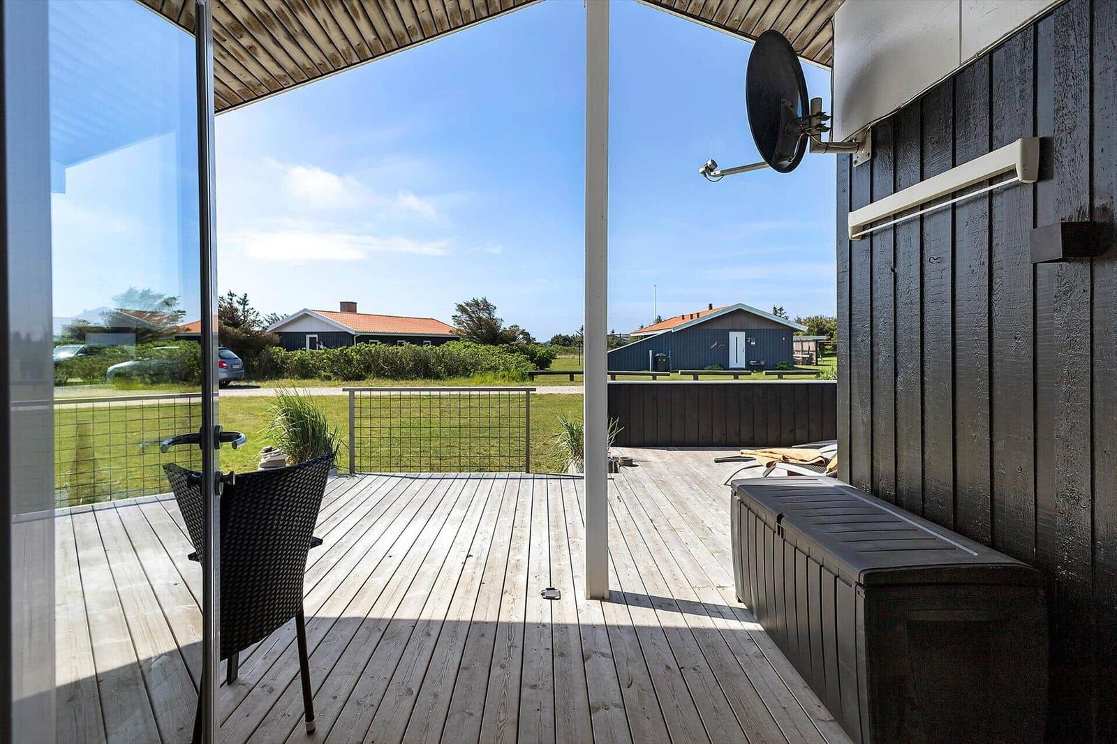 Terrasse mit Holzboden, Sitzgelegenheit und Blick auf Grünfläche und Häuser.