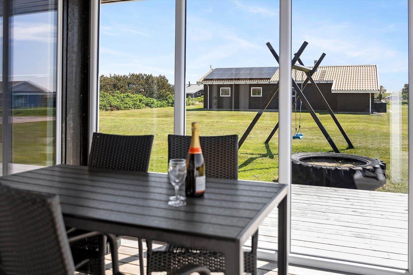 Terrasse mit Tisch und Stühlen. Blick auf grünen Garten und Haus mit Schaukel.