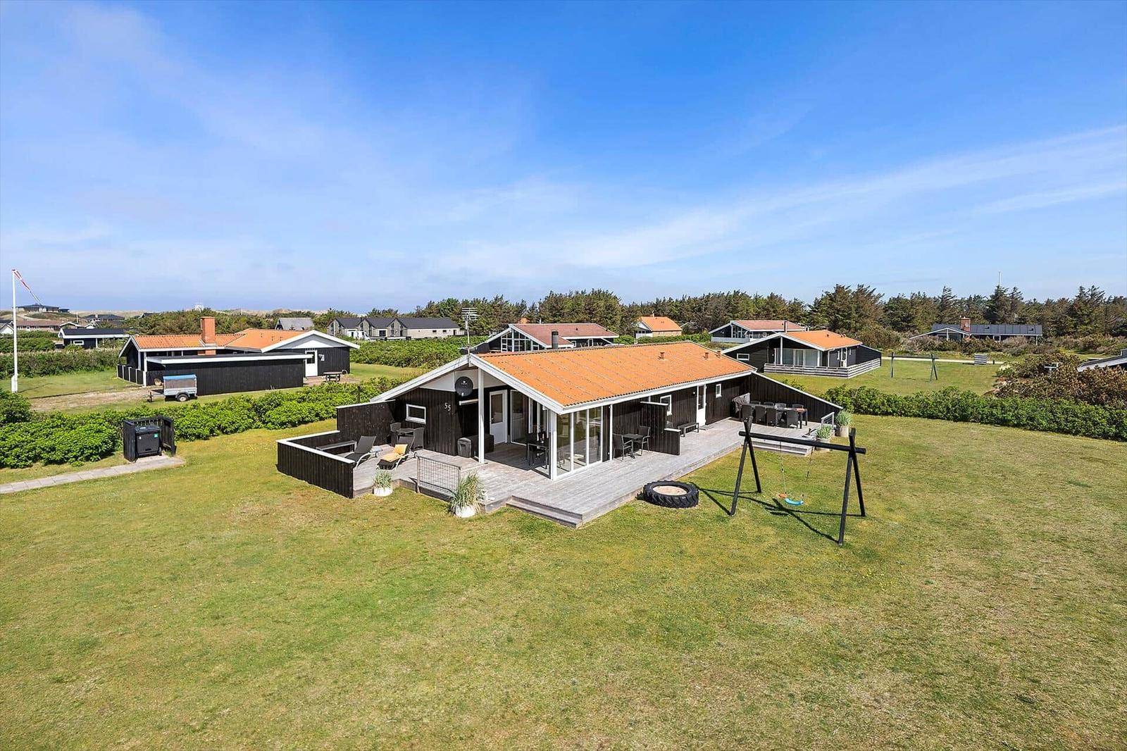 Haus mit Terrasse, Garten und Schaukel. Umgeben von Grün und weiteren Häusern.