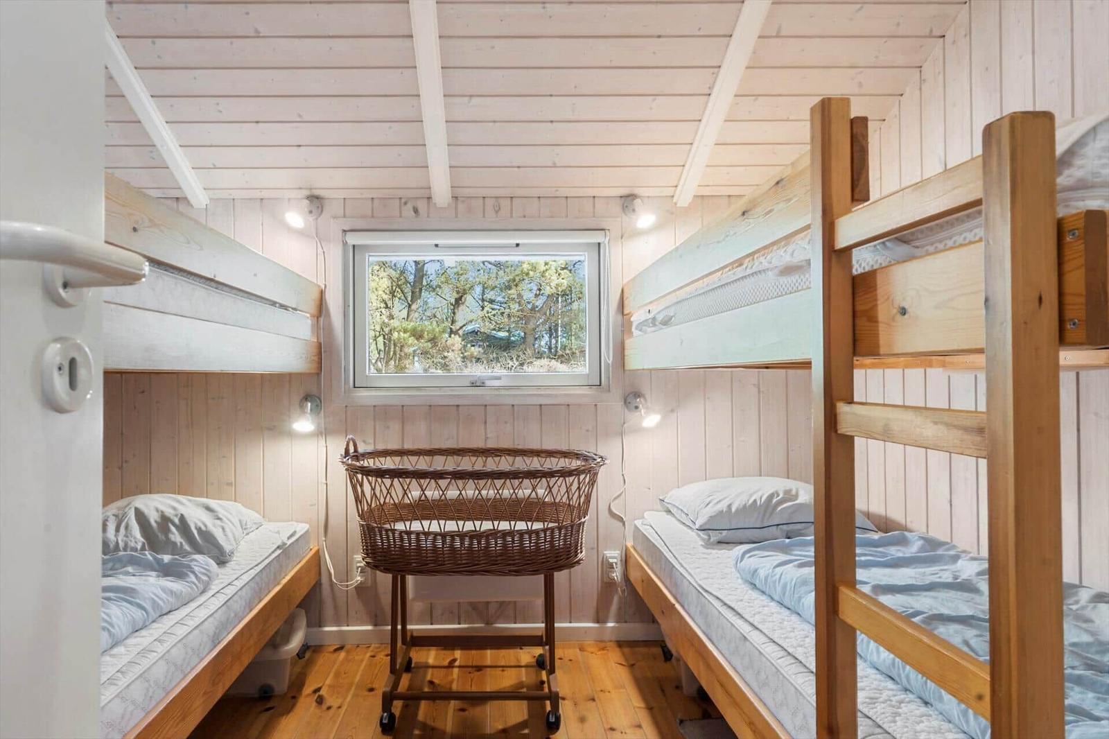 Zimmer mit zwei Etagenbetten und einem Wicker-Kinderwagen. Holzwände und -boden. Fenster mit Blick auf Bäume.