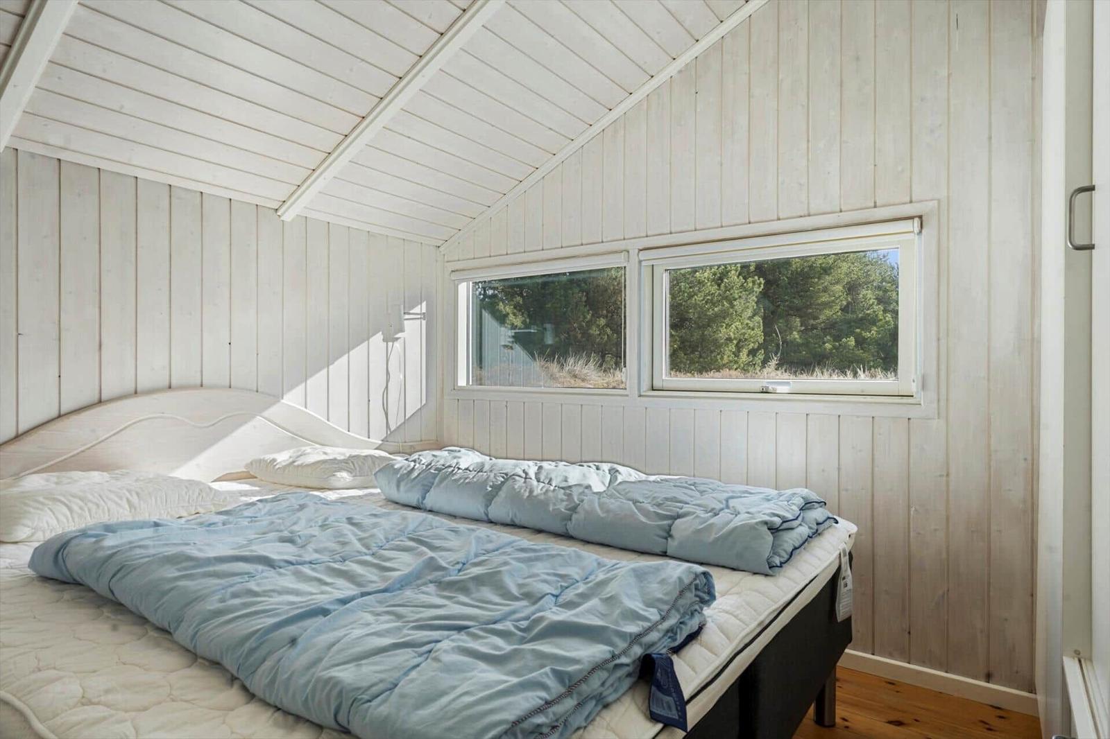Schlafzimmer mit Bett, Fenstern und Holzwandverkleidung.