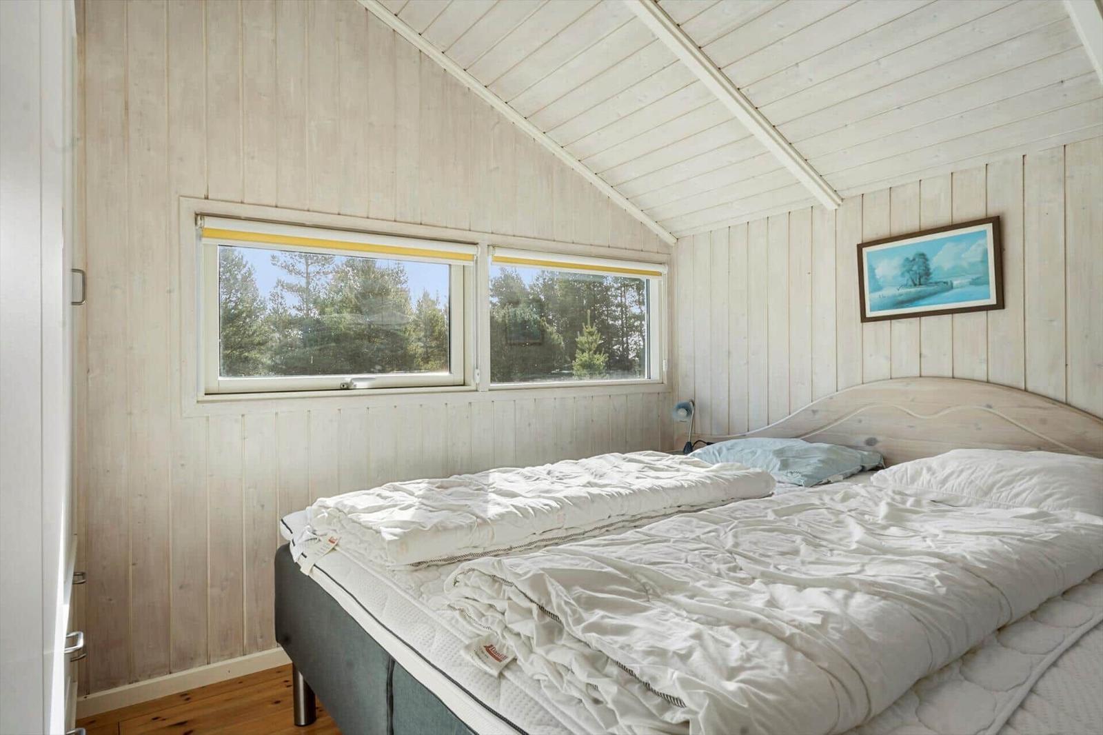 Schlafzimmer mit Bett, Fenster und Holzwandverkleidung