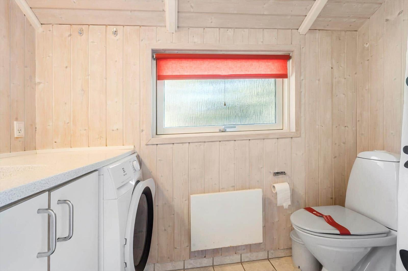 Badezimmer mit Toilette, Waschmaschine und Fenster mit rotem Rollladen.