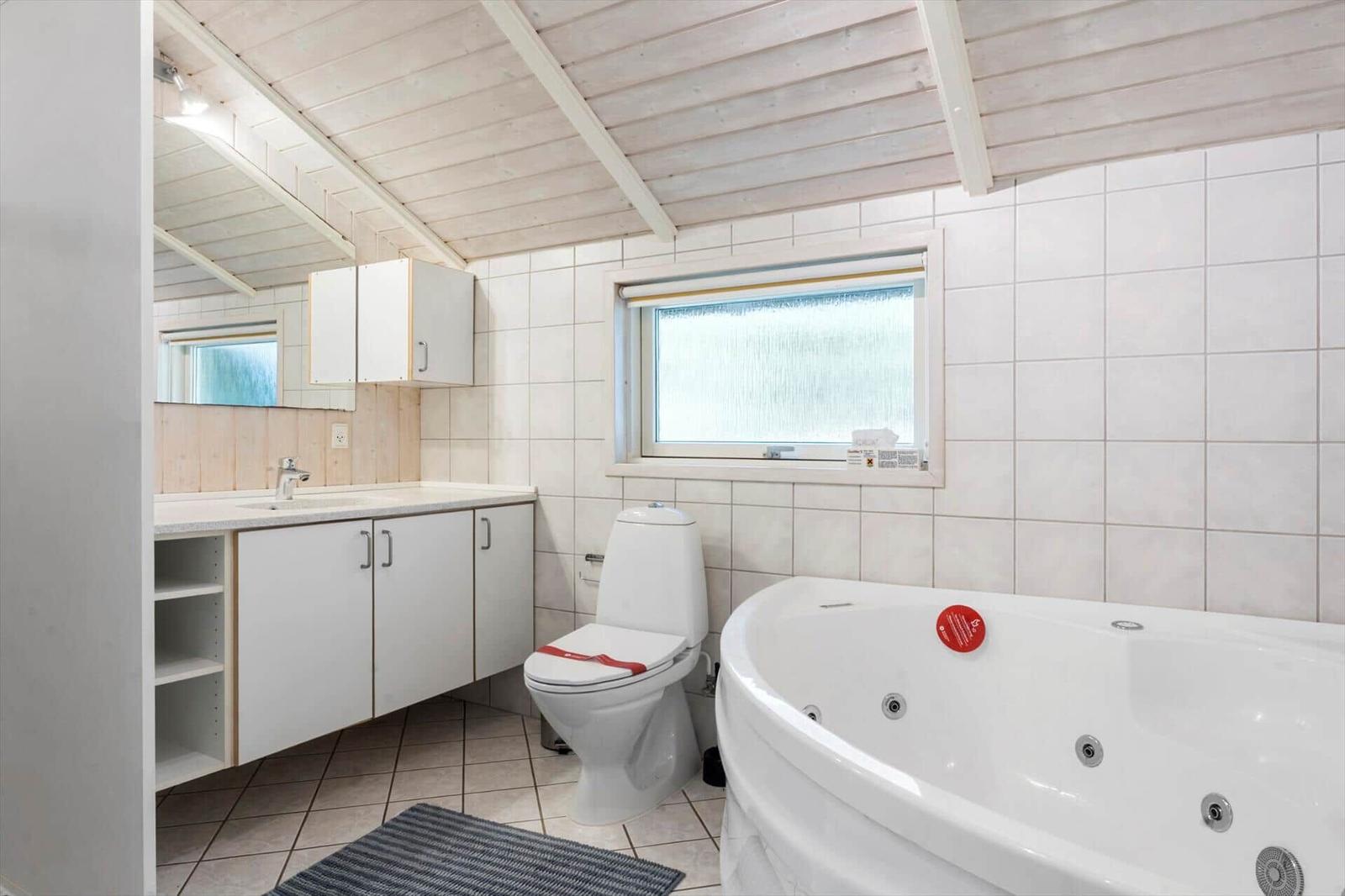 Badezimmer mit Badewanne, Toilette und Waschbecken unter Holzdecke.