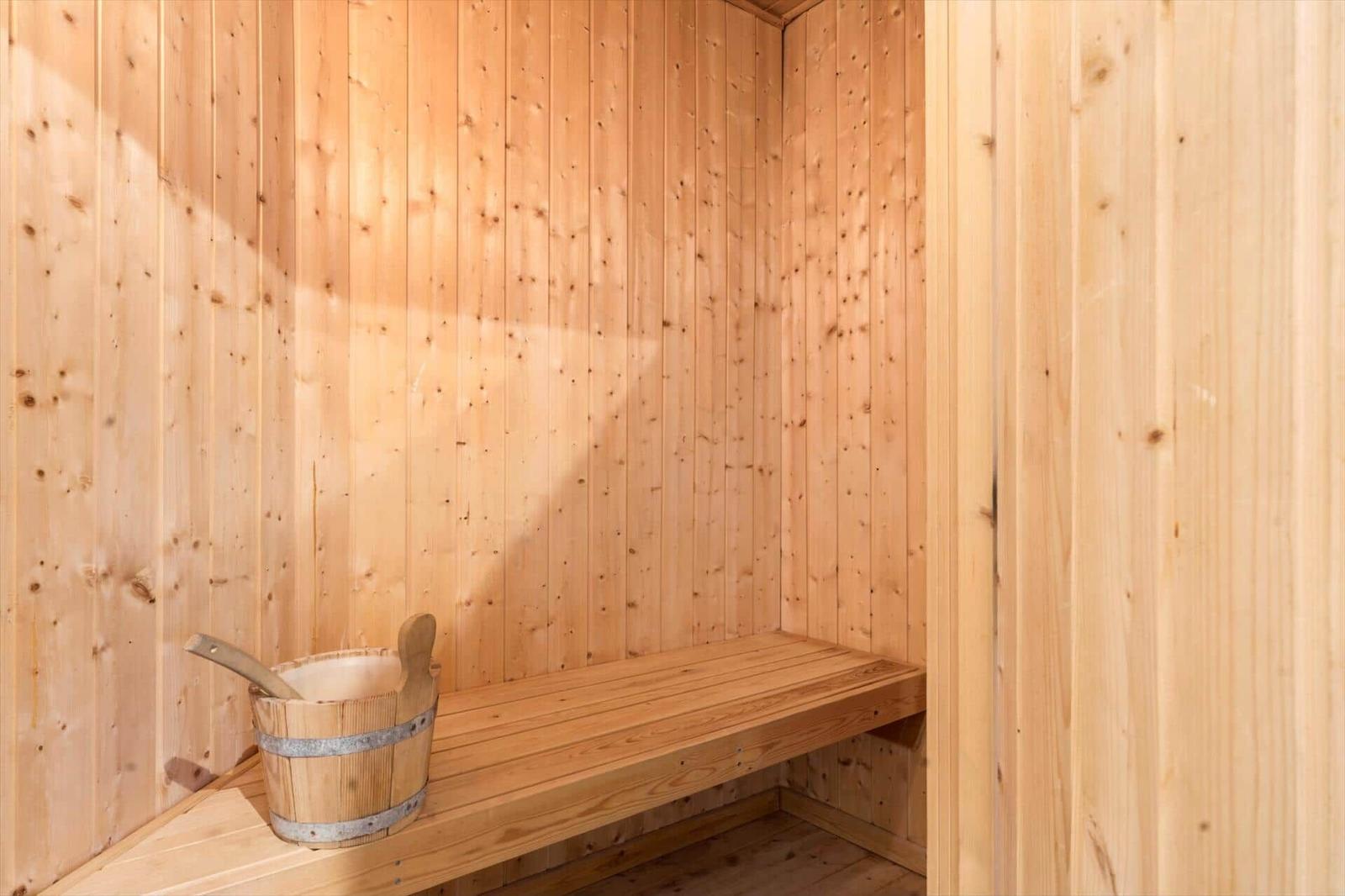 Sauna mit Holzwand und Sitzbank. Holzwaschbecken mit Löffel steht darauf.