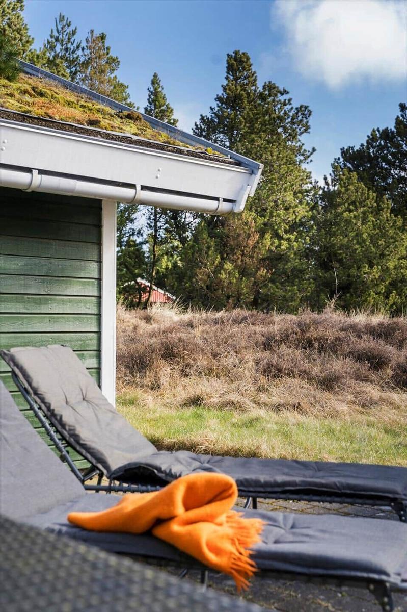 Terrasse mit Liegestühlen und orangefarbener Decke vor einem Haus mit Grasdach.