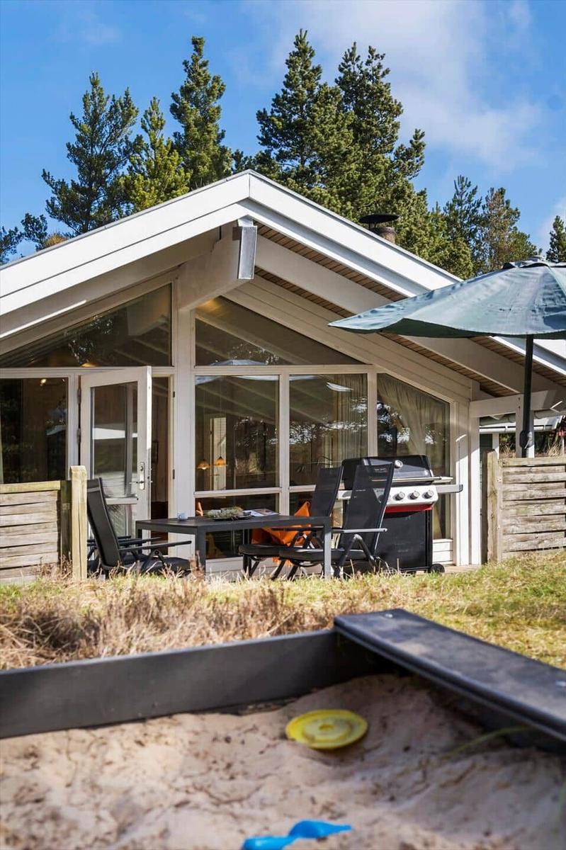 Modernes Haus mit Terrasse, Grill und Sandkasten im Vordergrund.