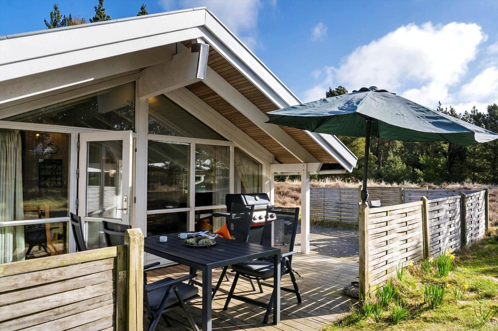 Terrasse mit Tisch, Stühlen und Sonnenschirm neben modernem Haus mit Glasfront.