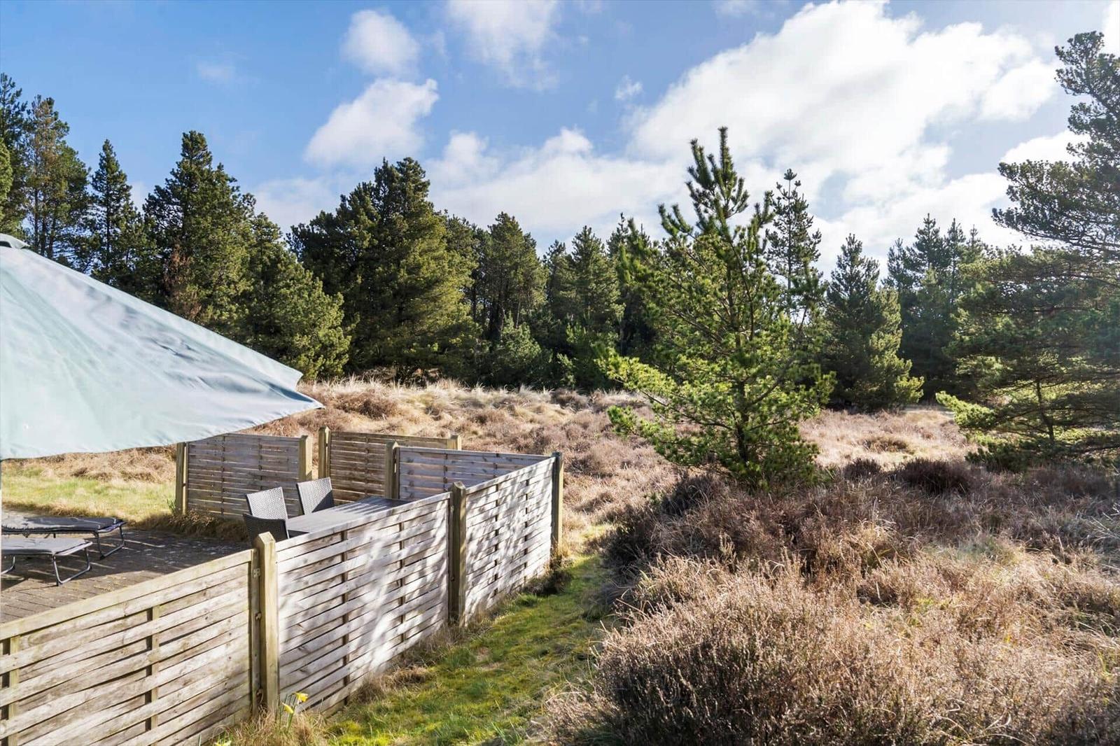 Terrasse mit Liegen und Sonnensegel. Umgeben von Holzgeländer und Wald.