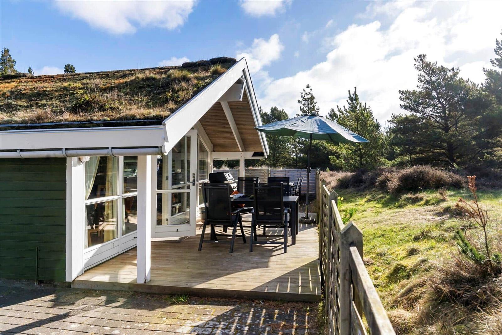 Haus mit grünem Dach, Terrasse mit Tisch, Stühlen und Sonnenschirm.