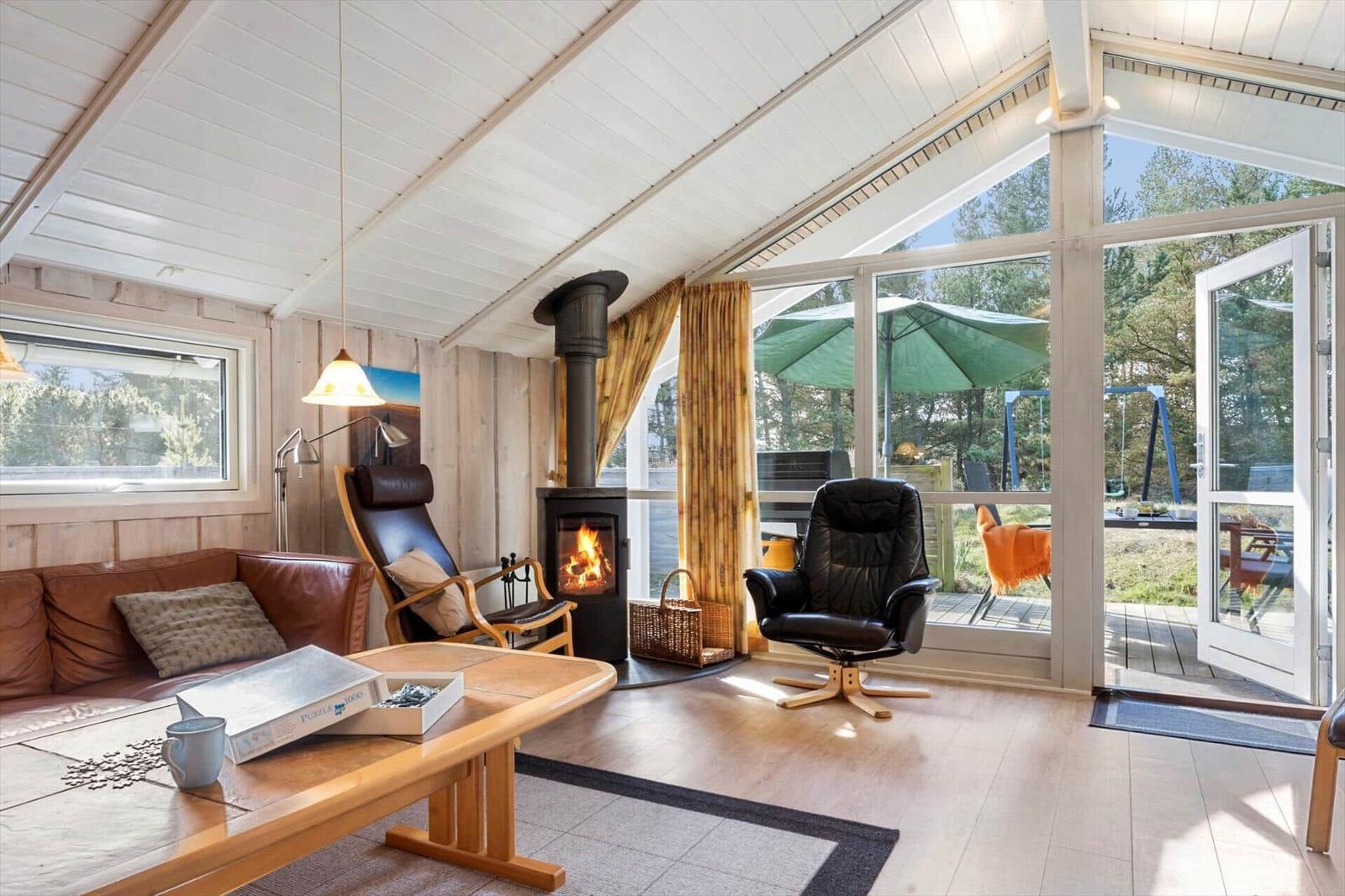 Wohnraum mit Kamin, Sofa, Sessel und Blick auf Terrasse mit Garten.