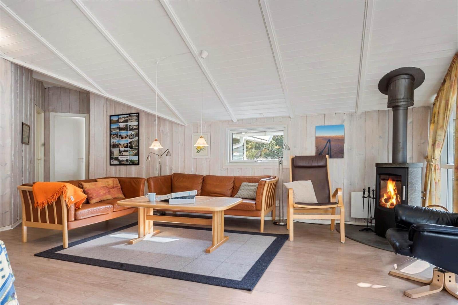 Wohnzimmer mit Sofa, Sessel und Kaminofen. Holzwände und Boden.
