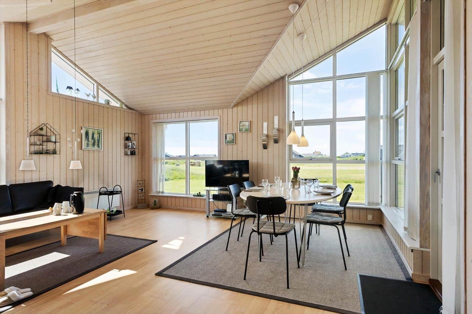 Wohn- und Essbereich mit Holzwand, großen Fenstern und moderner Einrichtung.