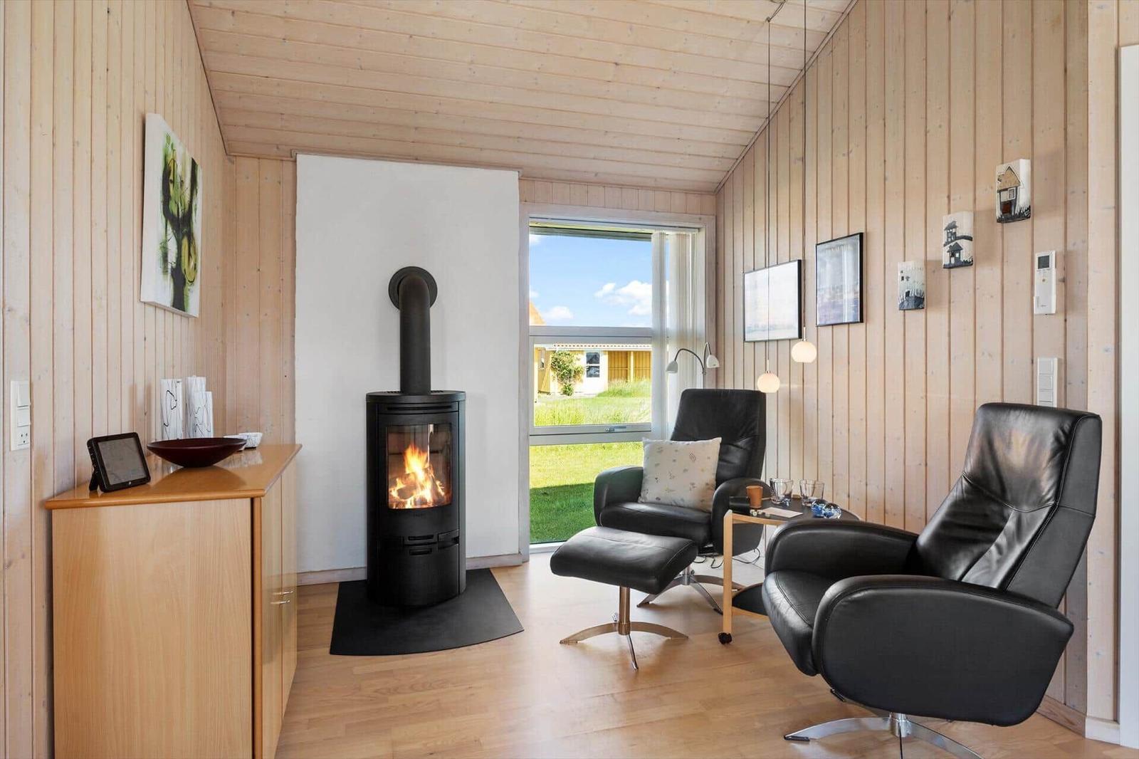 Ein Raum mit Holzwänden, Kamin und zwei schwarzen Sesseln vor einem Fenster.