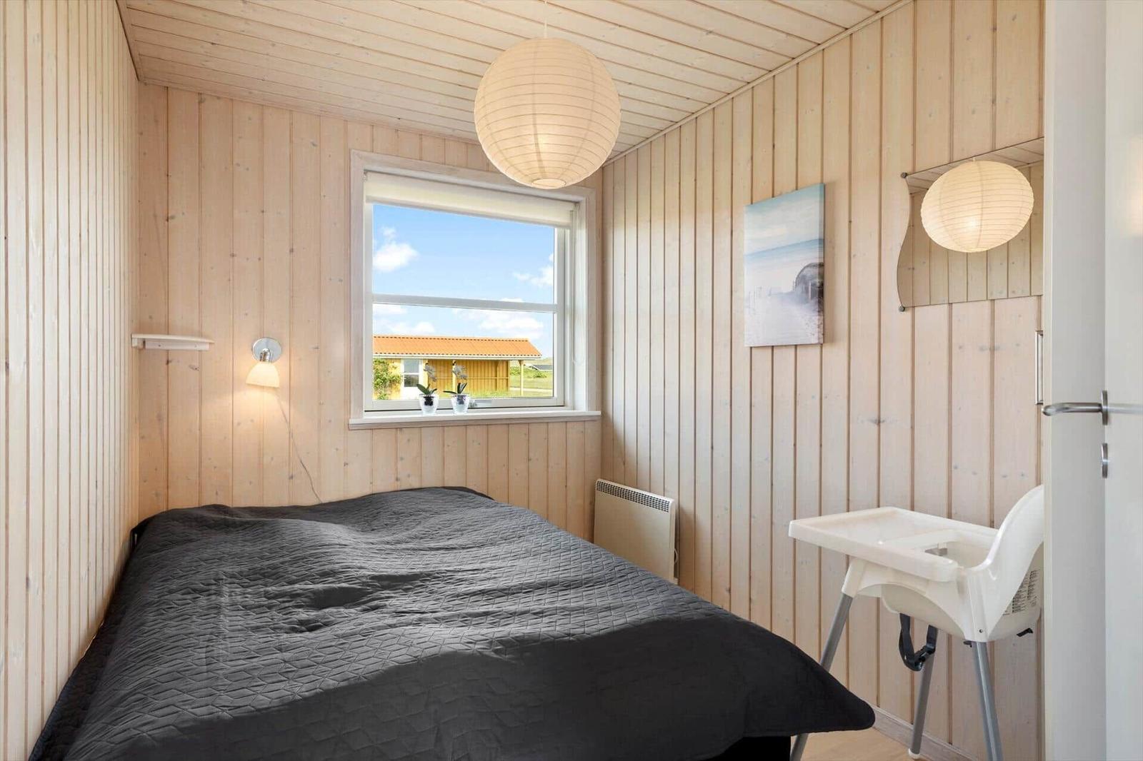 Schlafzimmer mit Bett, Fenster und Hochstuhl. Holzwände und Decke.