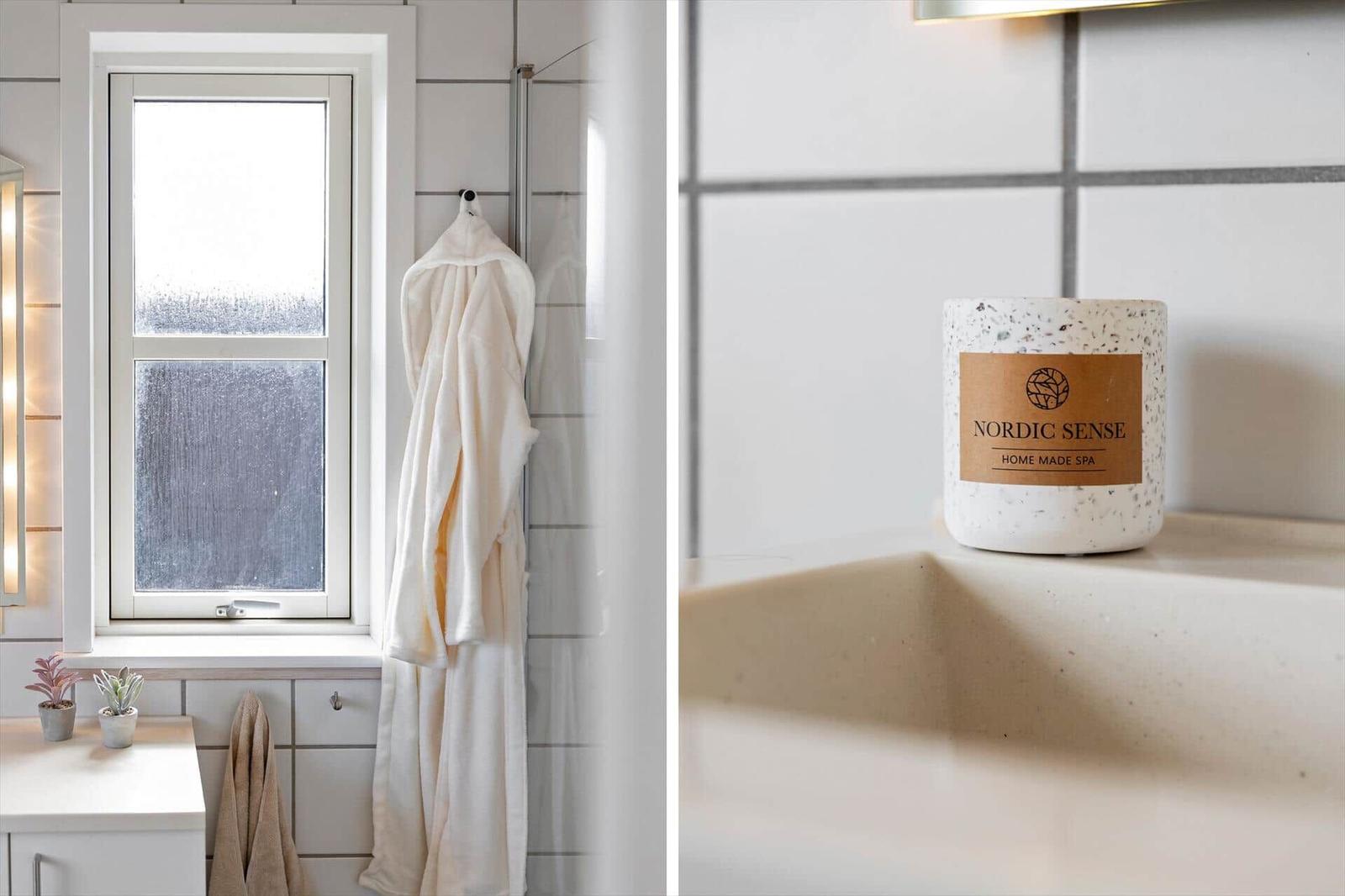 Badezimmer mit Fenster, Bademantel und Kerze auf Waschbecken.