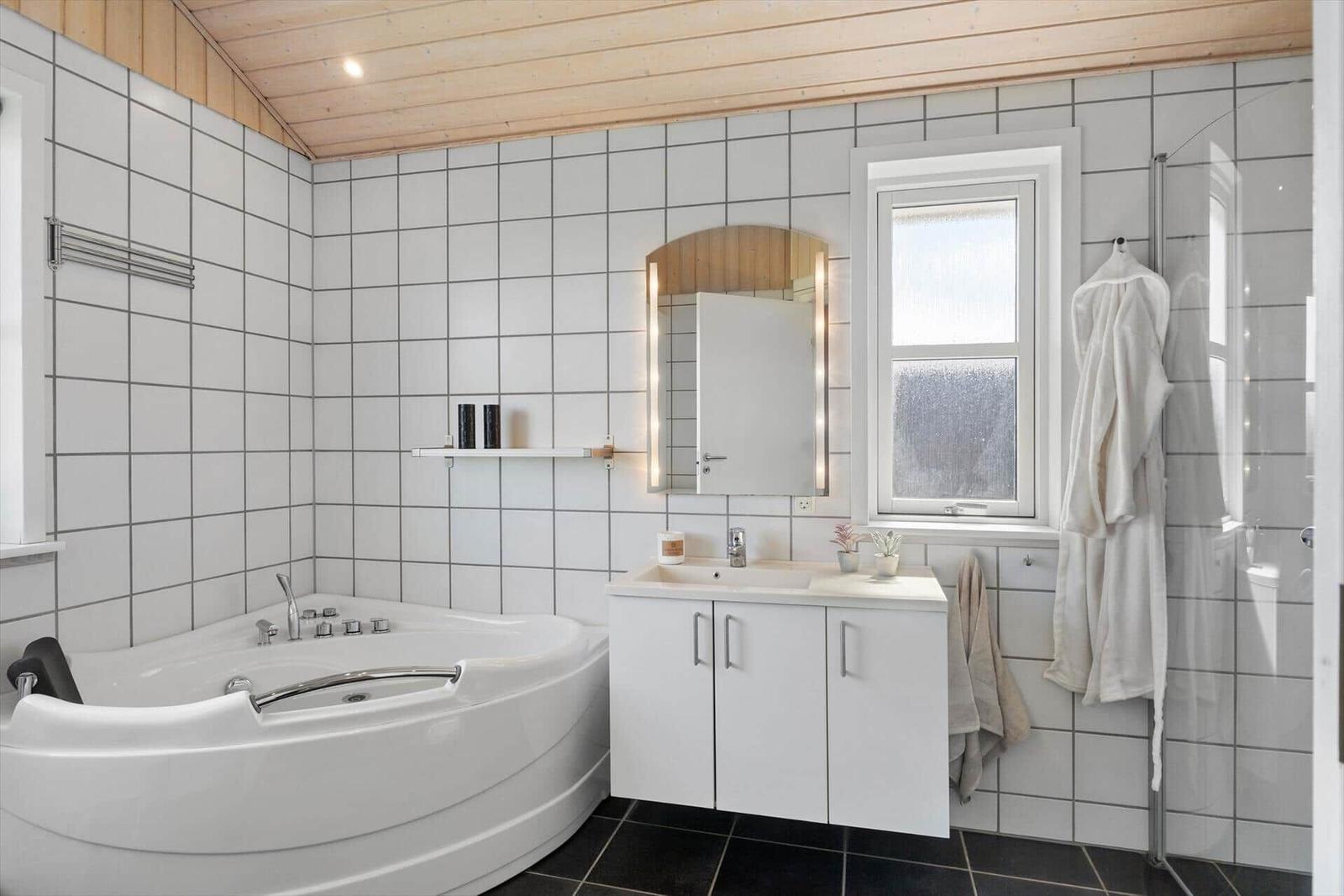 Bad mit Dusche, Waschbecken und Whirlpoolbad. Holzdecke und Fenster.