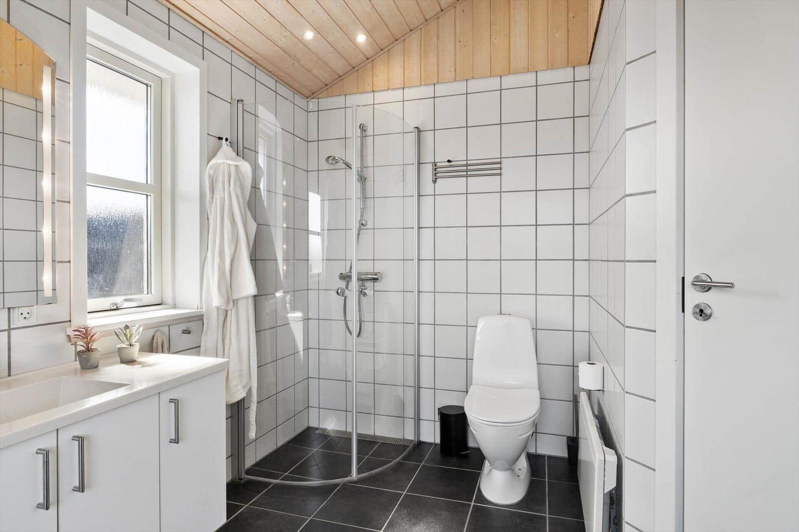 Badezimmer mit Dusche, Toilette und Waschbecken. Holzdecke und weiße Fliesen.