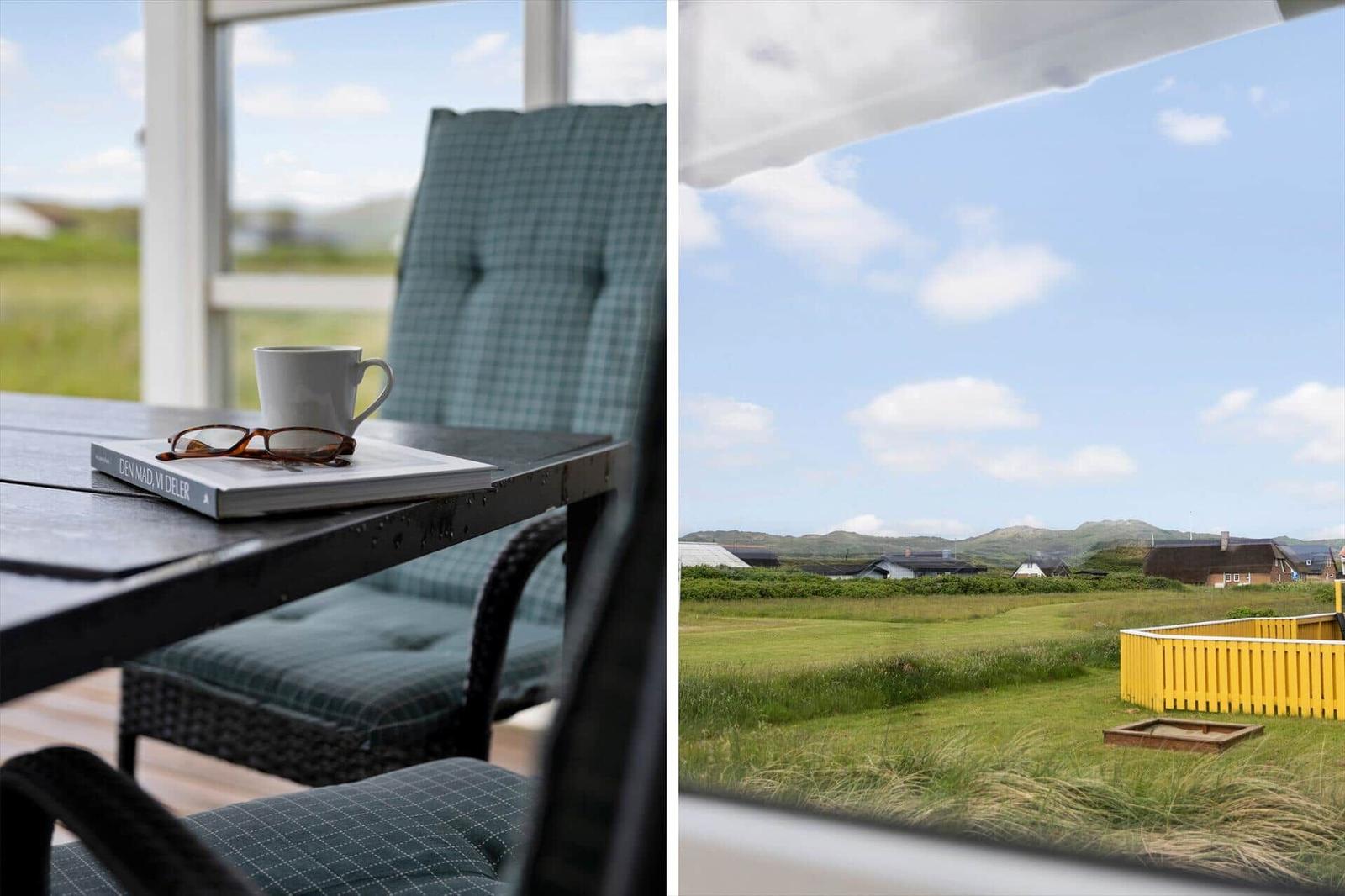 Tisch mit Tasse und Buch vor Fenster. Blick auf grünes Feld und Häuser.