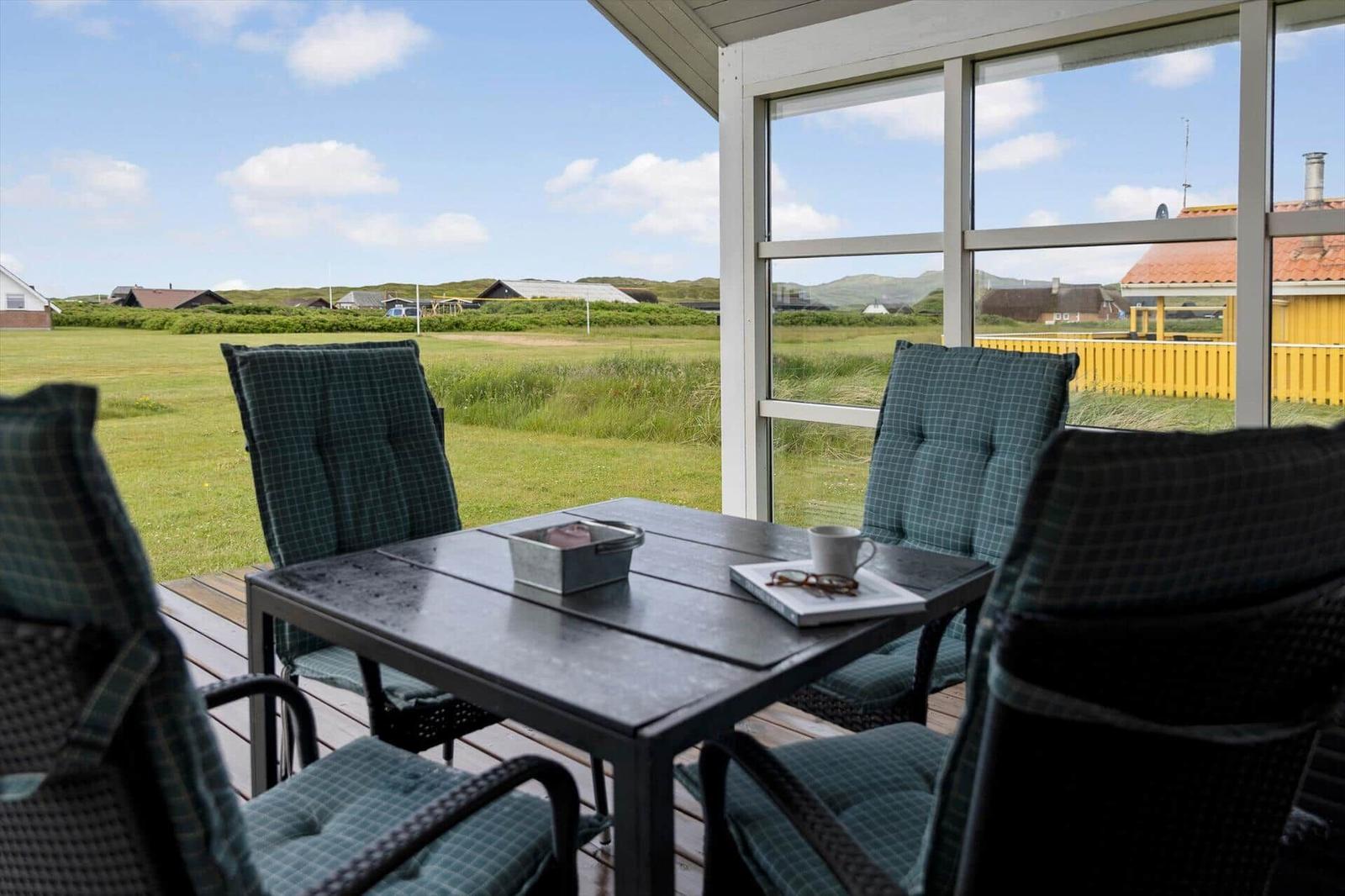 Terrasse mit Tisch und Stühlen, Blick auf grünes Feld und Häuser.