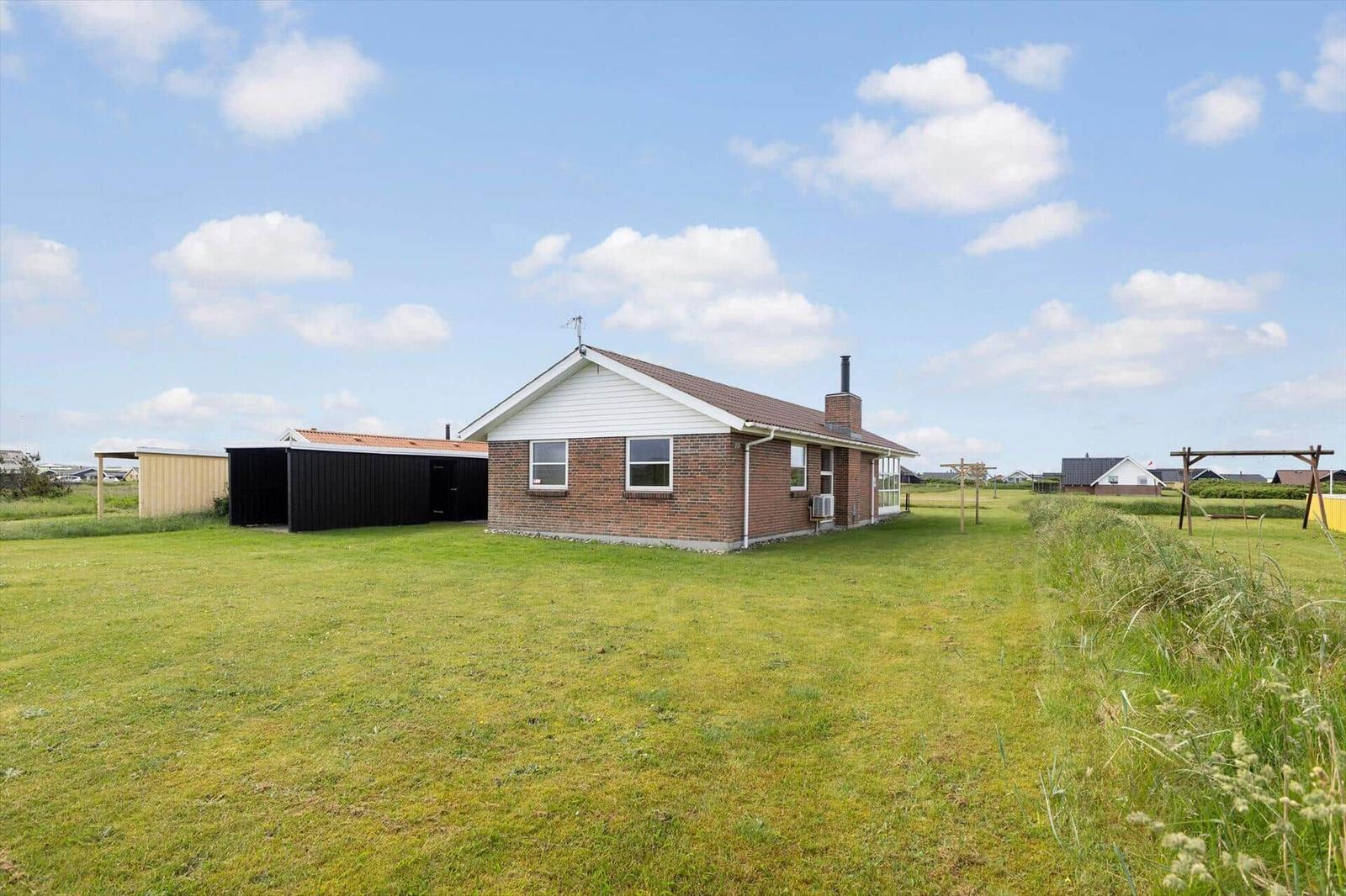 Ein Haus mit Backsteinfassade und weißem Dachansatz steht auf einer grünen Wiese.
