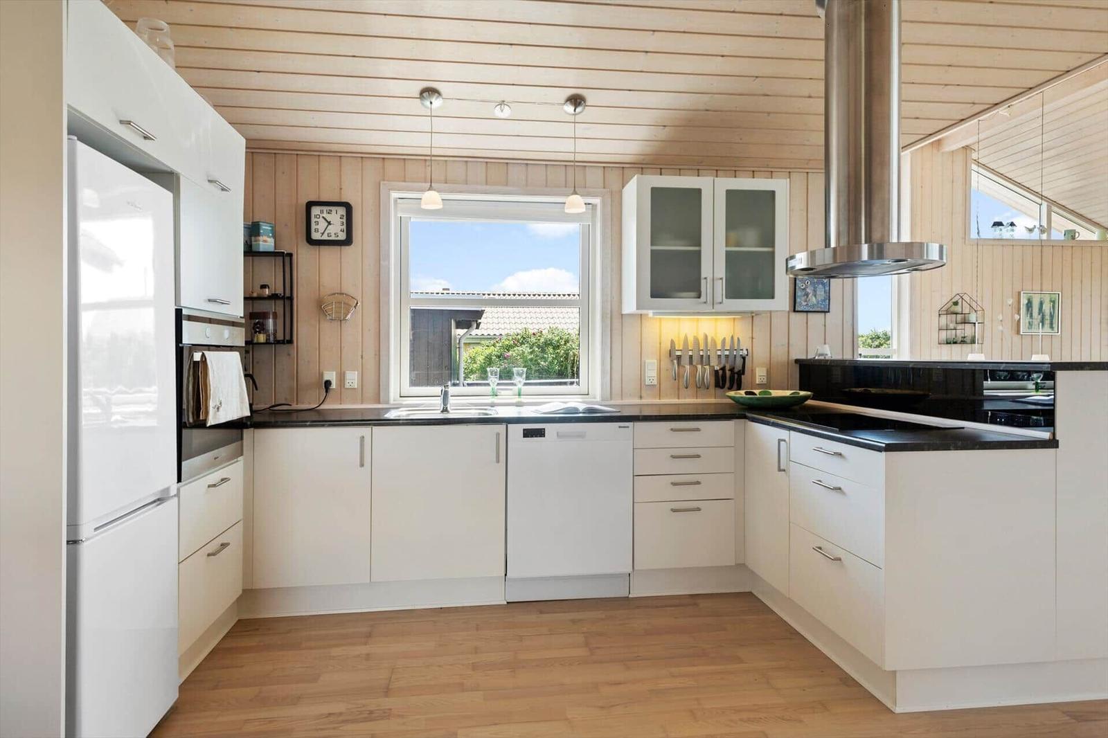 Küche mit weißen Schränken, Holzboden und Fenster zum Garten.