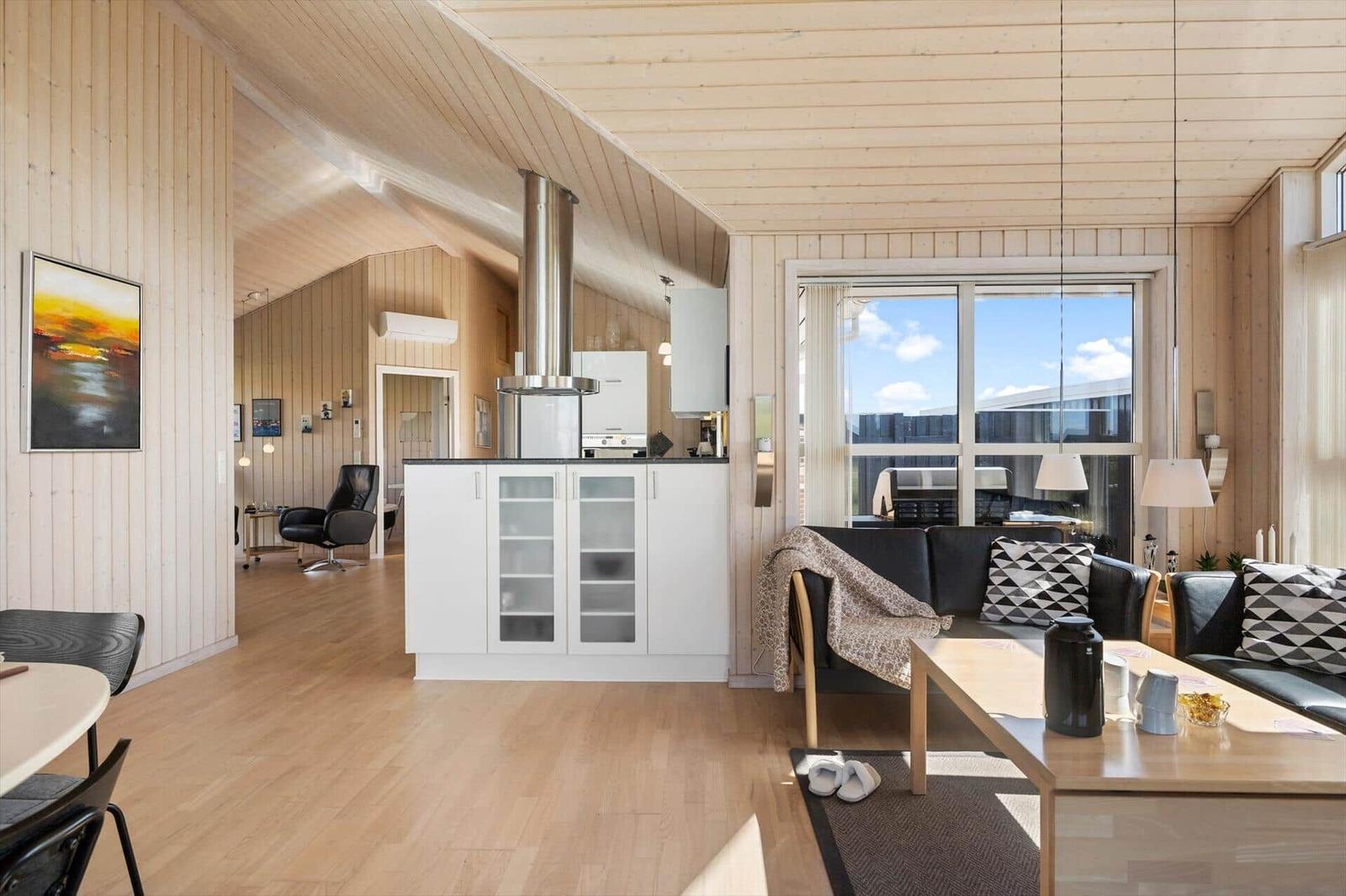 Wohnung mit Küchenzeile, Sofa und großem Fenster. Holzdecke und -wände.