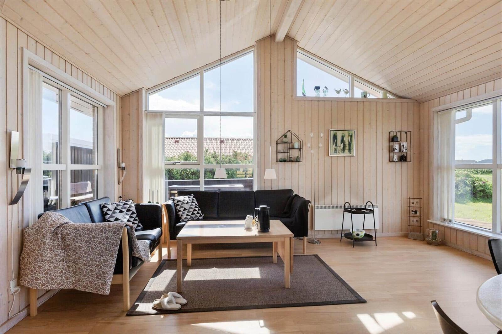Wohnzimmer mit Holzwänden, großem Fenster und schwarzen Sofas.