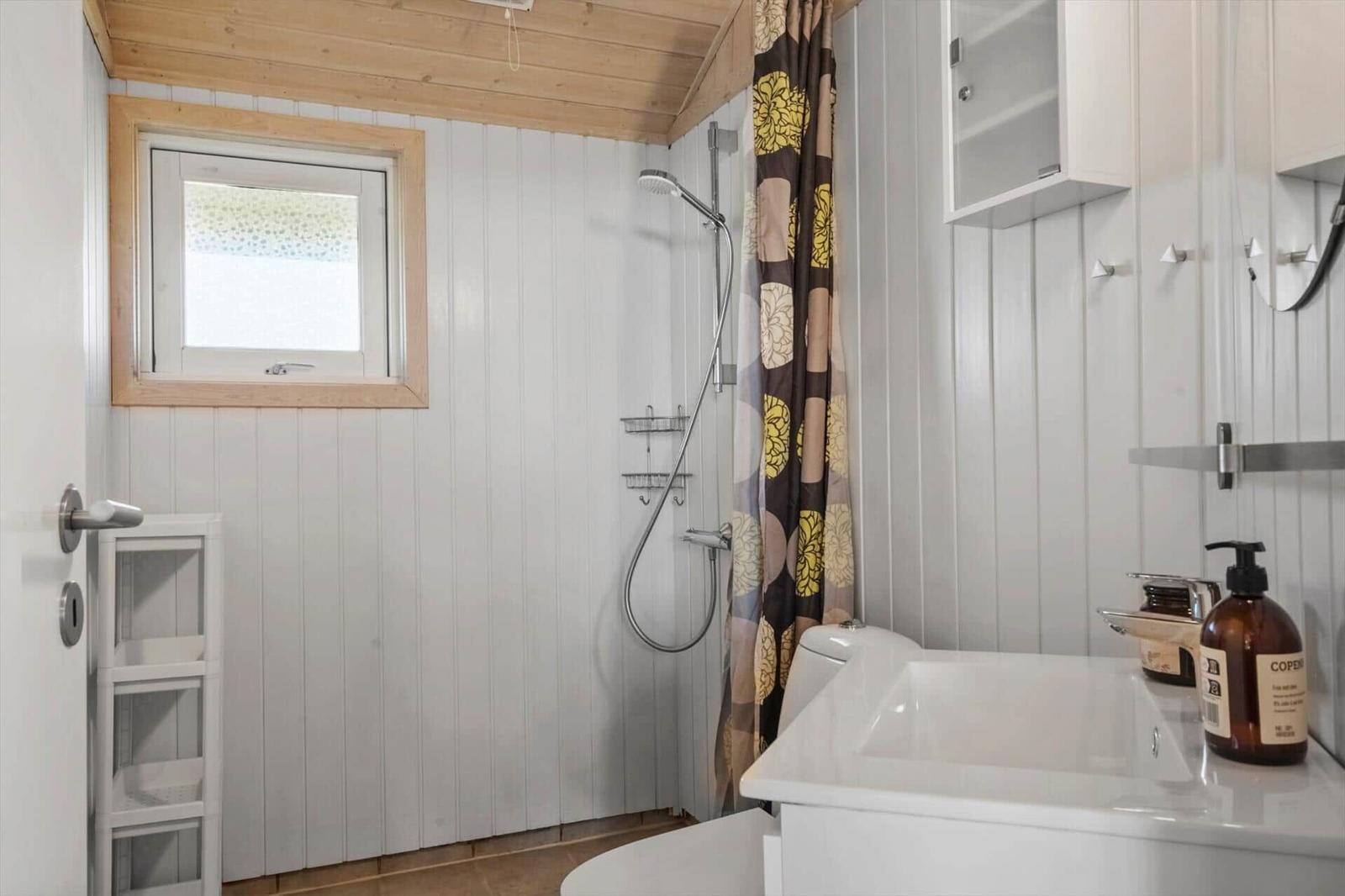Badezimmer mit Dusche, Waschbecken und Fenster.