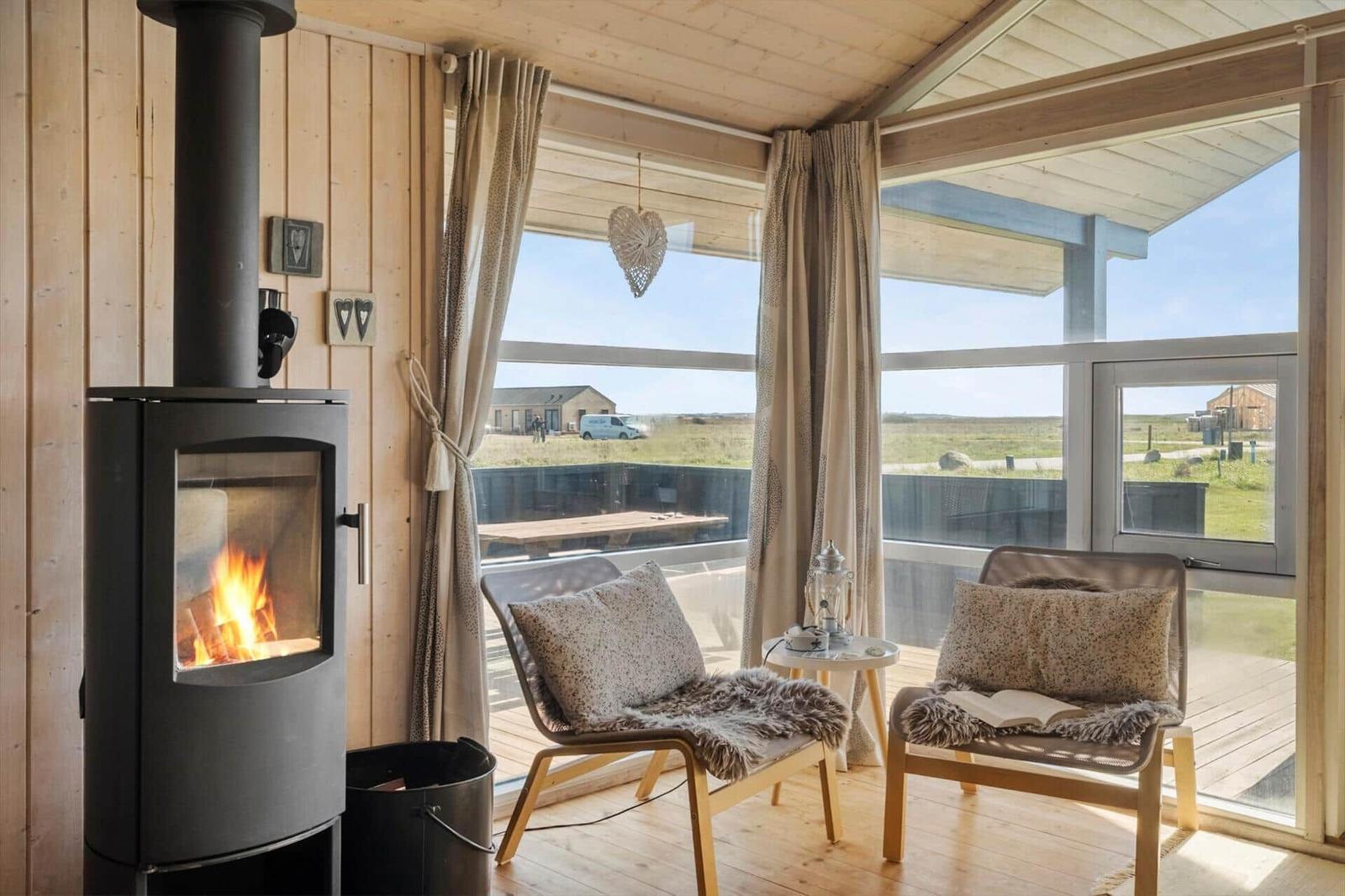 Raum mit Kamin, zwei Sesseln und großem Fensterblick auf die Landschaft.