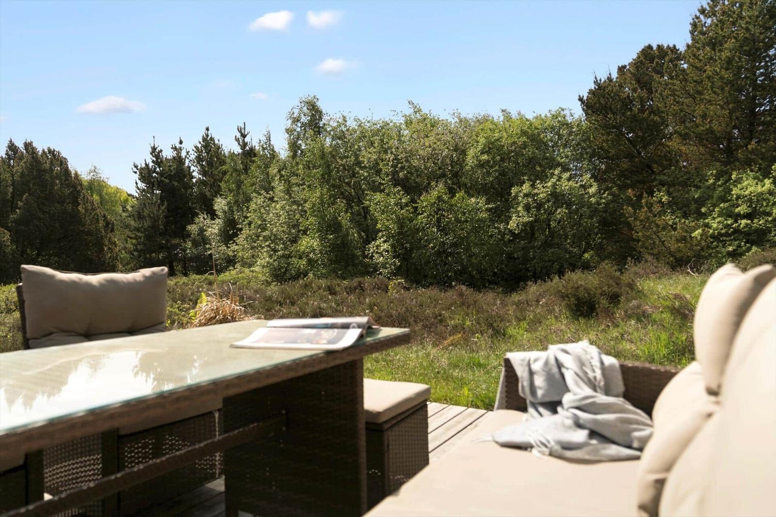Terrasse mit Tisch und Sitzgelegenheiten, Blick auf einen Wald.
