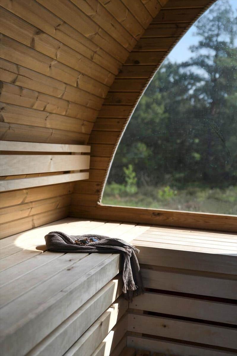 Holzsauna mit großem Fenster und Sitzbank. Außenseite zeigt Wald.