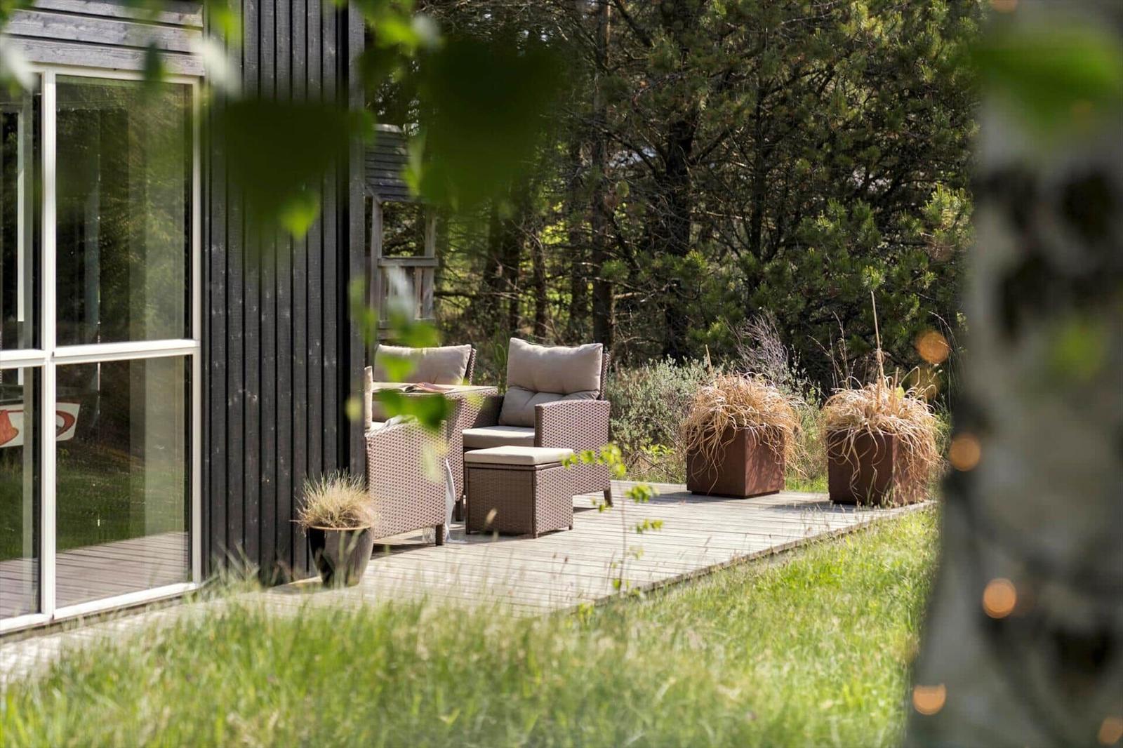 Terrasse mit Sitzgruppe, Pflanzen und Blick in den Wald.