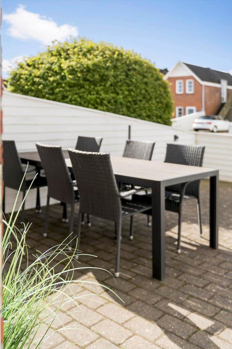 Terrasse mit Tisch und sechs Stühlen auf gepflastertem Boden.