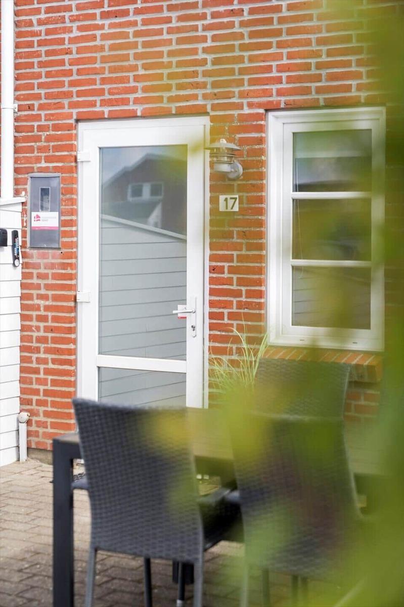 Haus mit rotem Backsteinfassade, weißer Tür und Fenster. Außenbereich mit Tisch und Stühlen.
