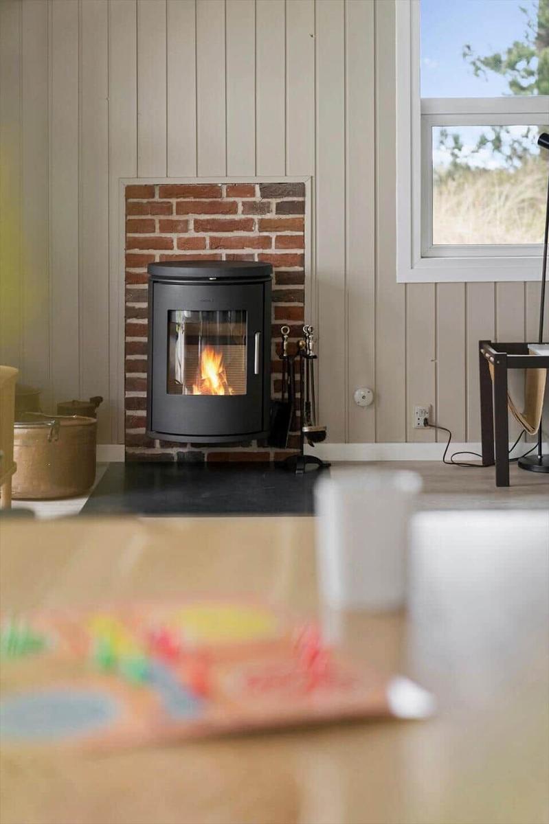 Kaminofen mit brennendem Feuer in einem Raum mit Holzwand und Fenster.