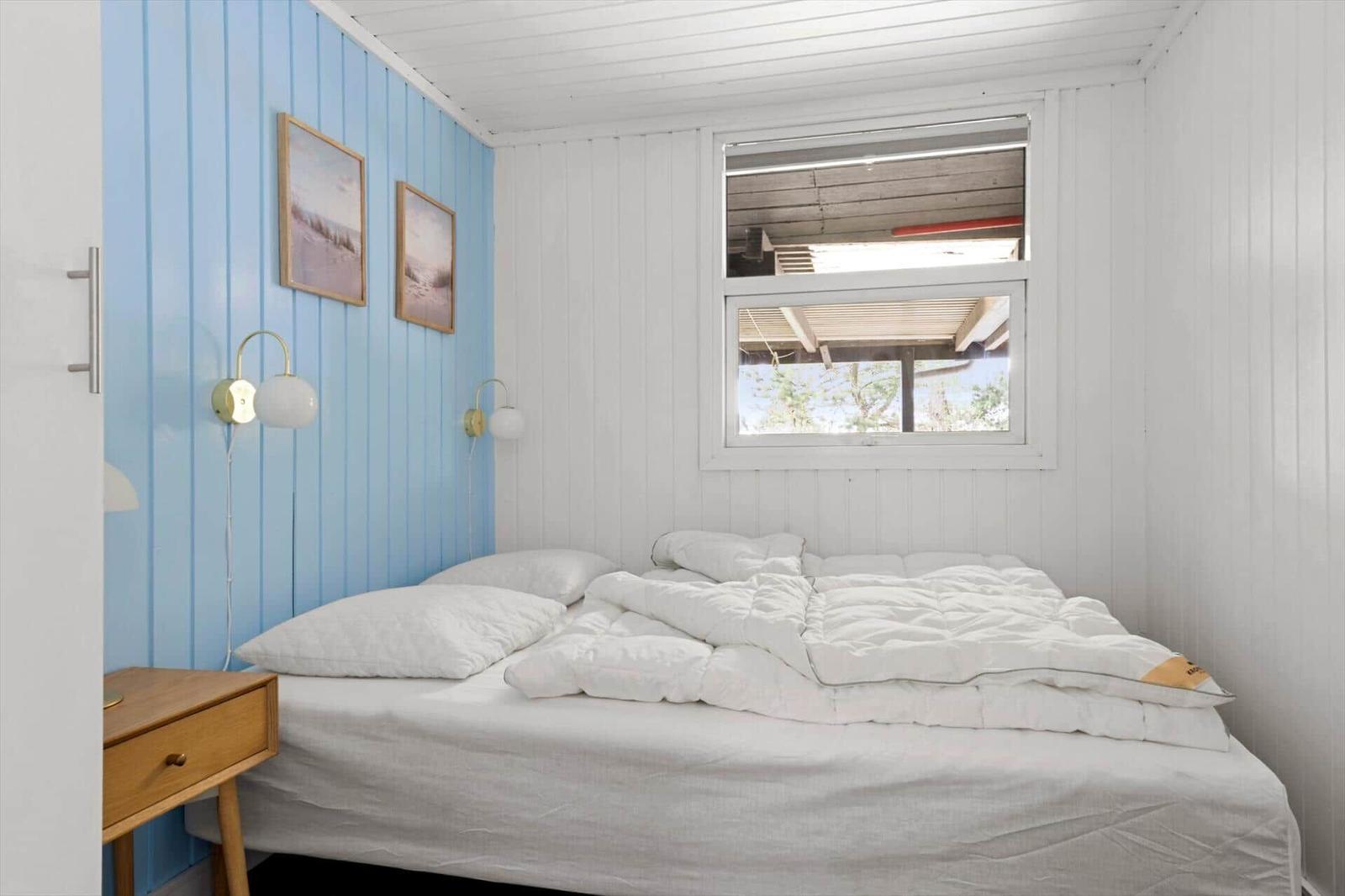 Schlafzimmer mit Bett, Fenster und blauer Wand. Nachttische und Wandlampen.