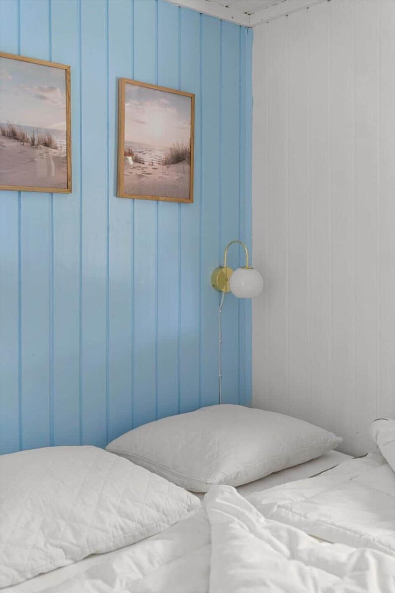 Schlafzimmer mit blauer Wand, zwei Bildern und einer weißen Bettwäsche.